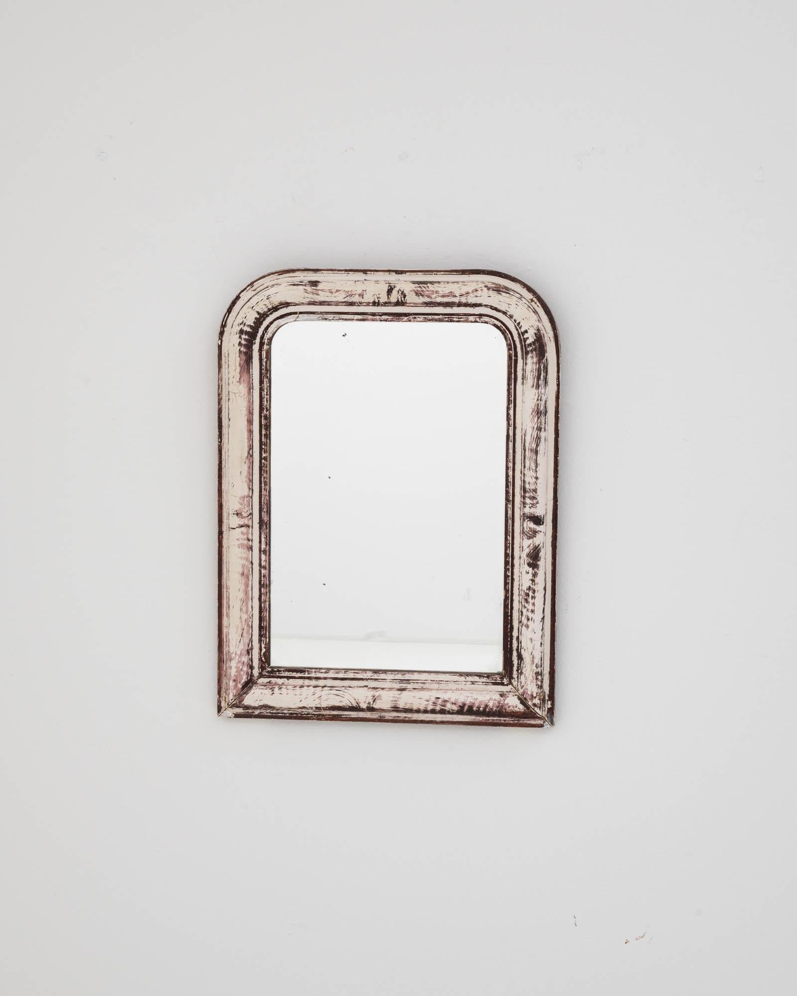 The 1900s French wood white patinated mirror presents an understated elegance that resonates with the shabby chic aesthetic. The distressed white paint reveals glimpses of the wood beneath, highlighting the mirror's journey through time and adding