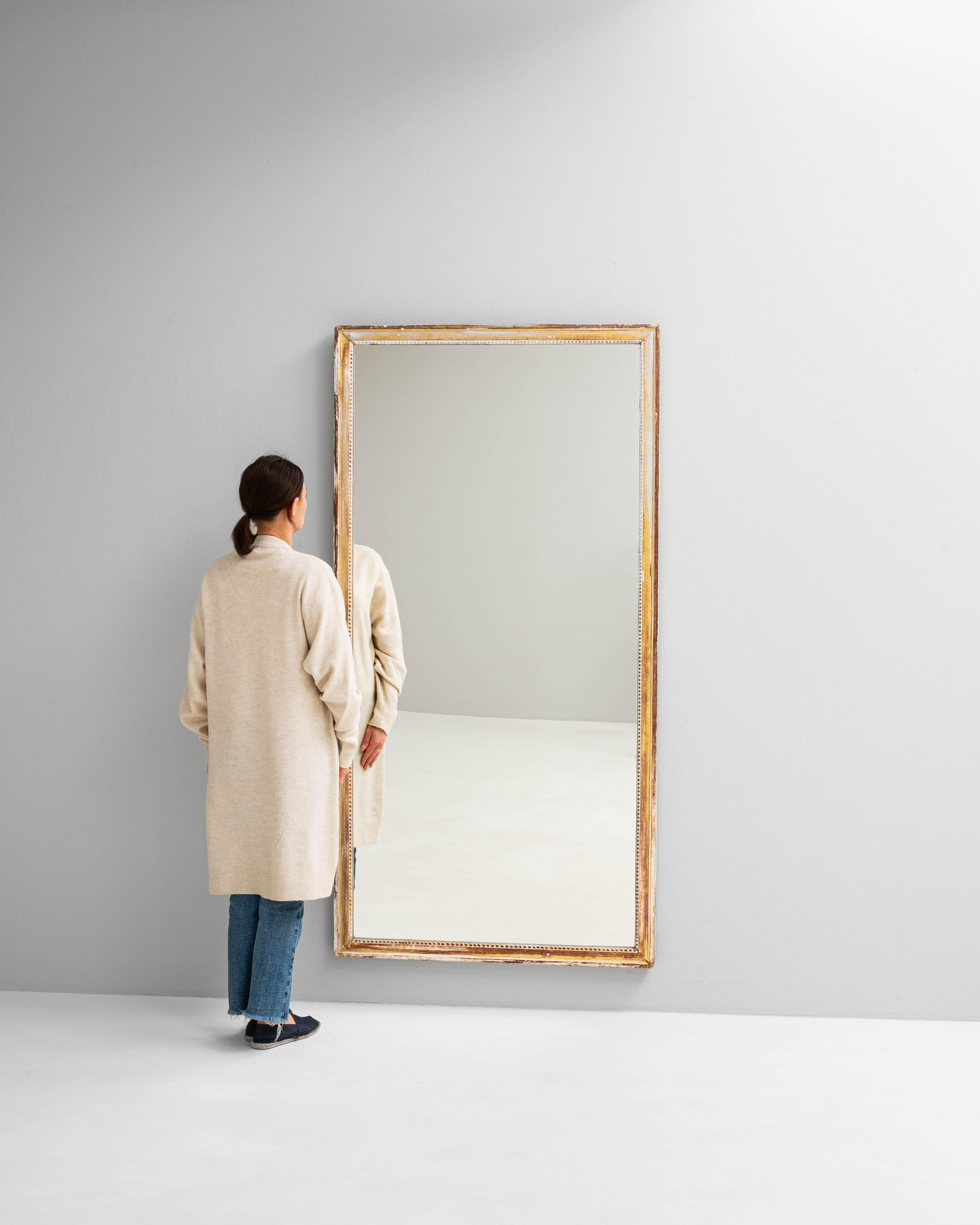 Questo specchio francese dei primi del Novecento presenta una forma rettangolare senza tempo, esaltata dalla cornice in legno patinato bianco tenue con sottili dettagli dorati. La finitura invecchiata e le delicate perline lungo il bordo interno