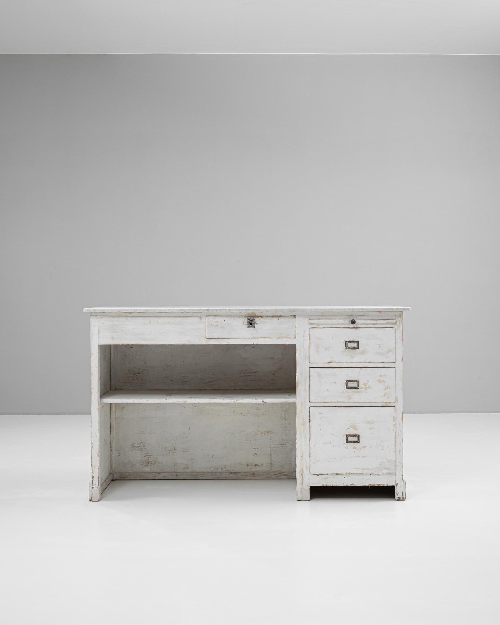 This early 20th-century French shop counter features a white patinated wooden frame and a solid marble top, offering both charm and durability. Its timeworn finish reflects years of use, adding character and authenticity to the piece. The counter is