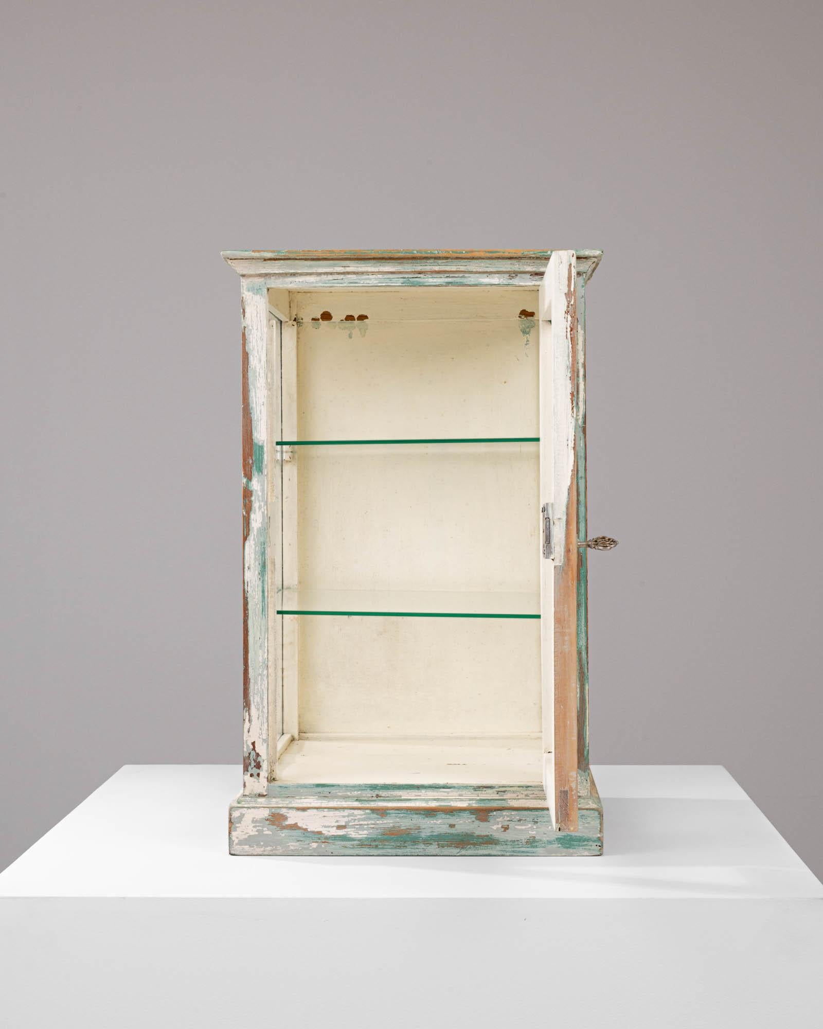 Step back in time with this charming 1900s French Wood White Patinated Small Vitrine, an enchanting piece that tells a story with its time-worn finish and delicate details. With its softly weathered white and seafoam green patina, this vitrine is a
