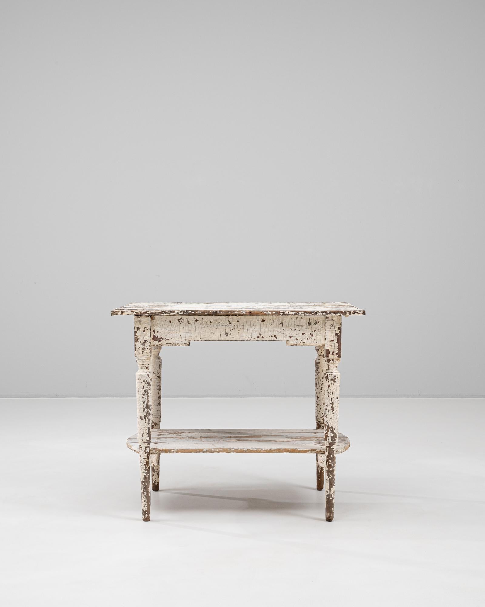 A charming example of early 20th-century French utility furniture, this wooden table features a beautifully distressed white patina that reveals layers of age and character. The rectangular top is supported by turned legs, lending a subtle