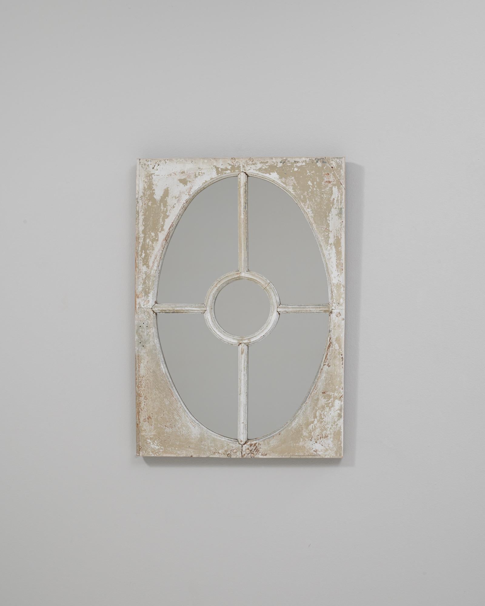 This 1900s French wood wall mirror features a beautifully worn white patinated finish that highlights its architectural charm and subtle decorative character. The frame showcases an elegant windowpane-style design with an elongated oval center