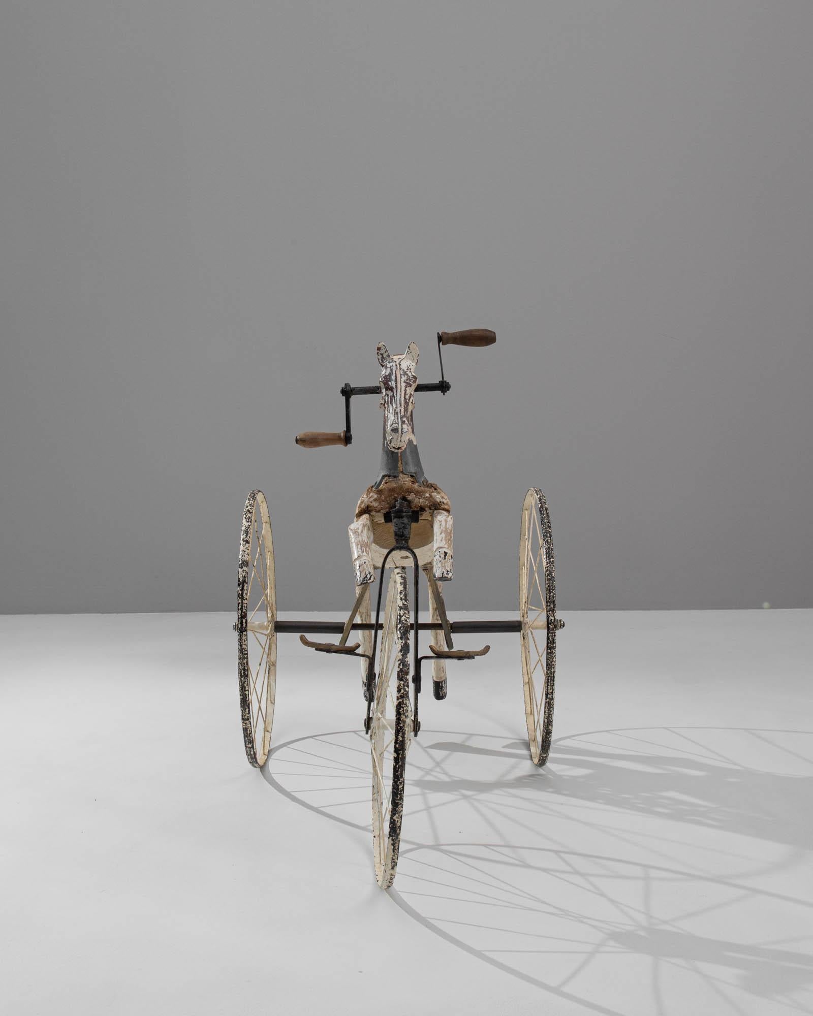 A wooden and metal horse tricycle created in France circa 1900. Vibrant yet seasoned and matured, this sprung horse glides on metal wheels that roll it gracefully into modernity. Through the passing of time, the white paint that coats both the