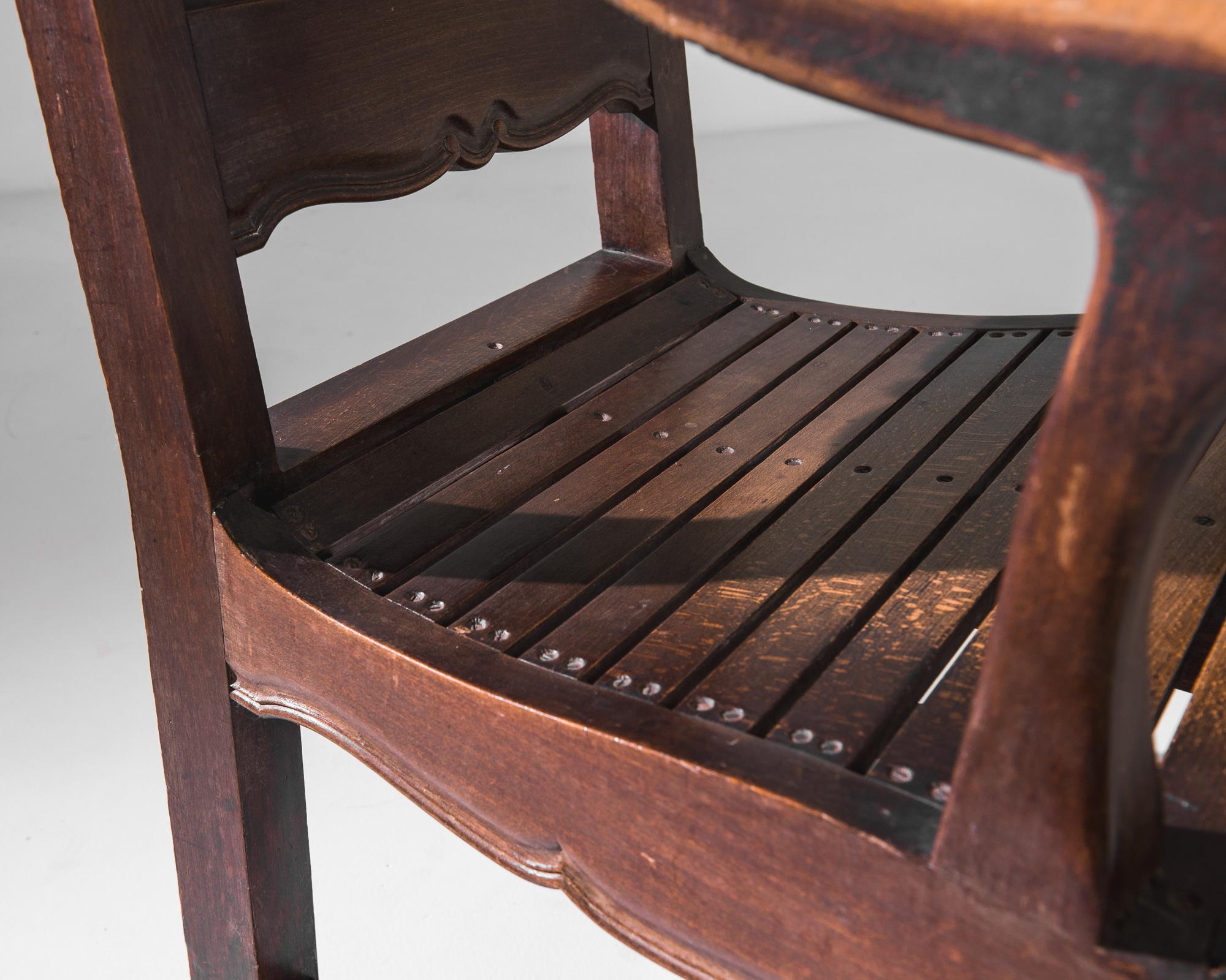Fauteuil en bois créé en Belgique au début du 20e siècle. Avec son dossier haut et sa dignité, ce somptueux fauteuil rayonne d'une aura d'autorité royale. Des tabliers somptueusement sculptés, des pieds latés et un dossier à panneaux témoignent d'un
