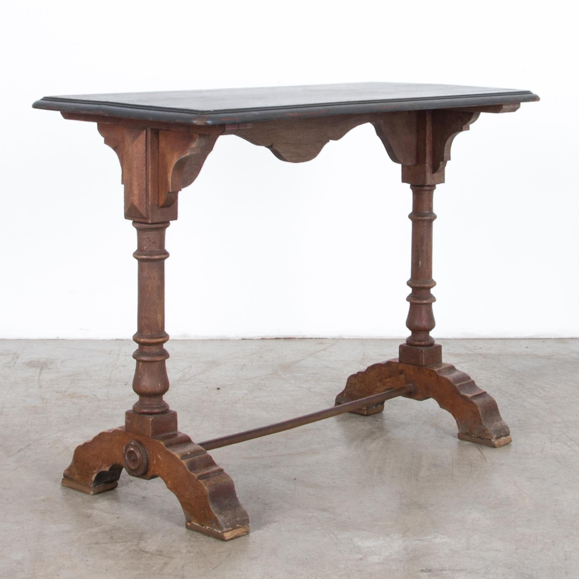 This charming 1900s French wooden bistro table perfectly captures the essence of Parisian café culture. The tabletop, painted in a sophisticated matte black, contrasts beautifully with the warm wooden tones of the base. Intricate carvings and the