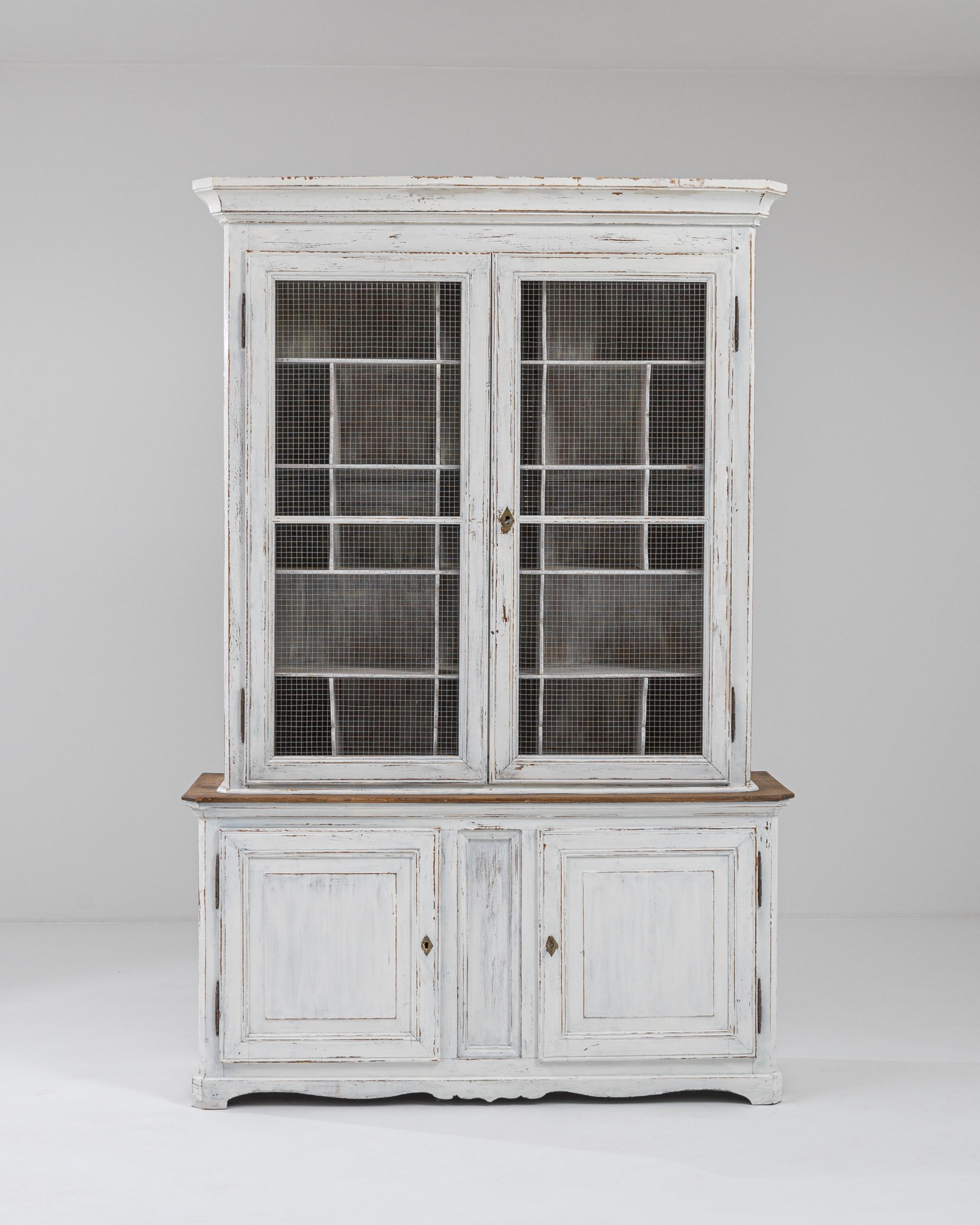 A wooden vitrine made in 1900s France. Featuring an array of cubbies in the upper cabinet, as well as two lower doors, this cabinet offers ample storage space. The upper doors are outfitted with a mesh screen, allowing for airflow. A pleasing patina
