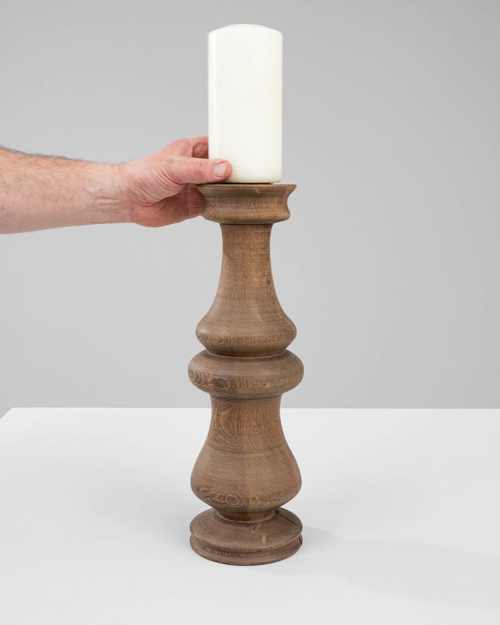 This 1900s French Wooden Candlestick is a beautifully turned piece of craftsmanship that brings with it the timeless appeal of natural wood. Each contoured segment, masterfully shaped, reveals the distinct rings and grain of the wood, bearing