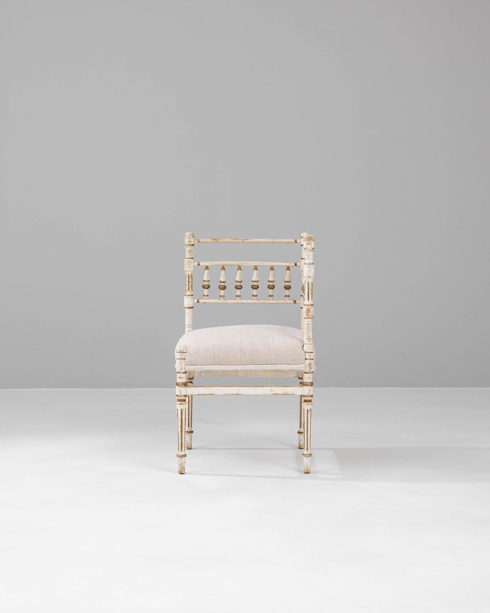 Capture the allure of French design with this 1900s Wooden Chair, a piece that speaks volumes of its storied past with every delicate chip and crack in its antique white paint. The chair's turned balusters and fluted legs are reminiscent of the