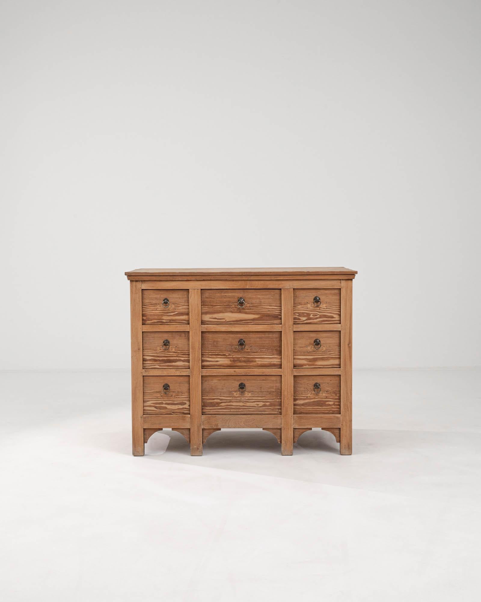 This 1900s French Wooden Chest of Drawers exudes classic elegance and utilitarian charm. Constructed from solid wood, its natural grain is a testament to the timeless beauty and durability of traditional materials. Each of the nine smoothly