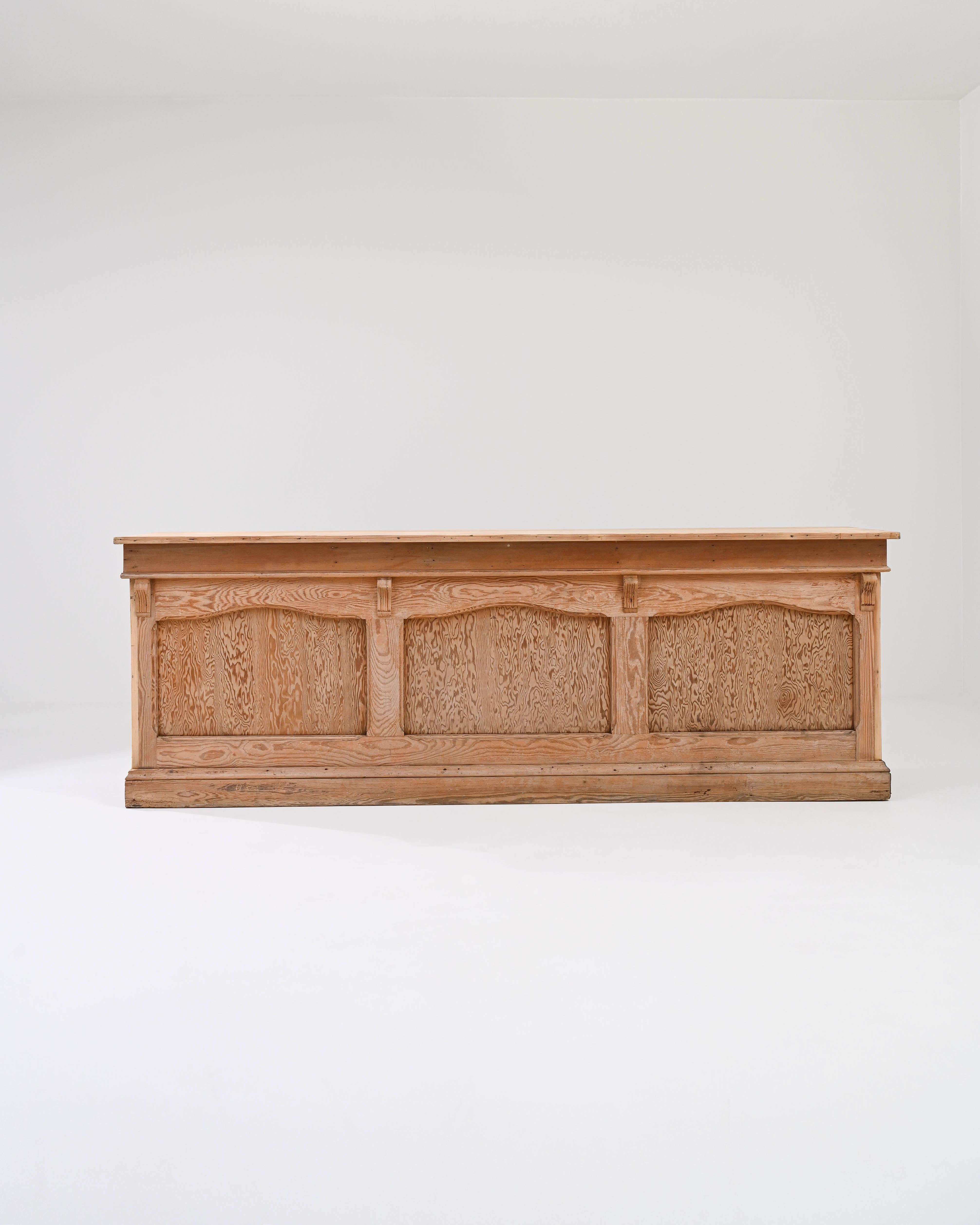 A wooden counter made circa 1900 and sourced in France. This expansive bar counter features four large compartments and two petite drawers. The natural wood grain that coats the buffet’s front paneling shimmers and swims in an almost psychedelic