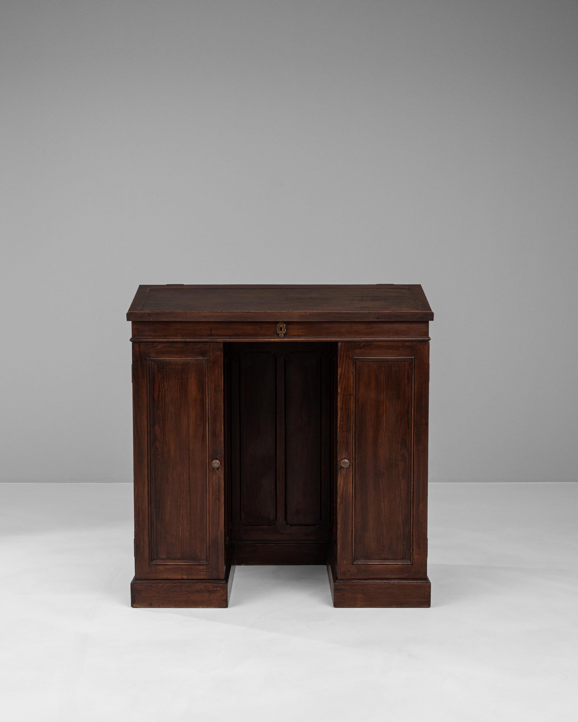Experience the rich history and craftsmanship of the early 1900s with this French wooden desk, an exemplar of classic design and functionality. Constructed from deep-toned wood, this desk features a distinctive hinged top that lifts to reveal a