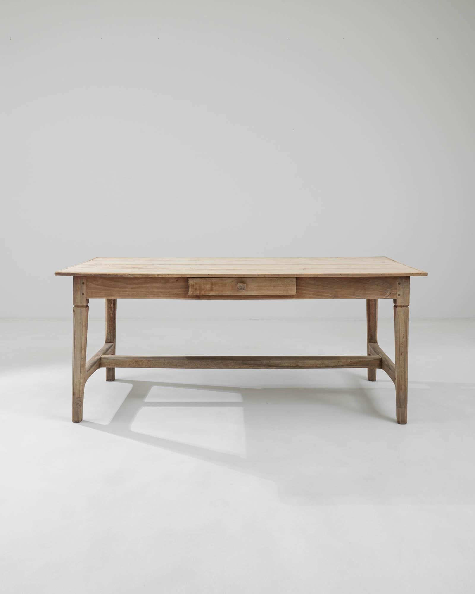 A wooden table created in 1900s France. This expansive dining table emits a cheery glow, both attractive as a rustic farmhouse piece and a minimalistic construction. Its colloquial charm stems from the mortise and tenon joints, dowel pegs, and other