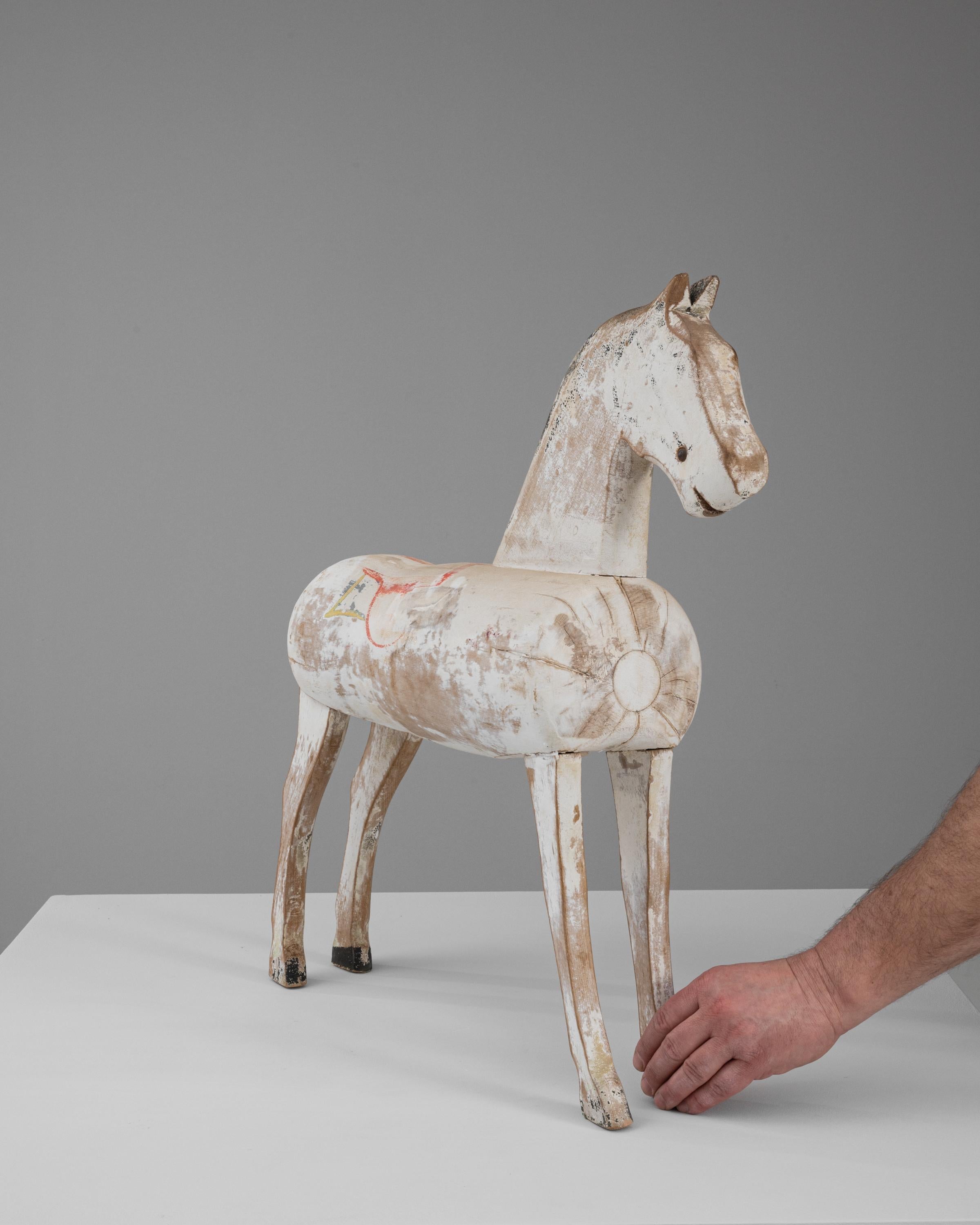 This 1900s French Wooden Horse is a splendid example of vintage craftsmanship and enduring folk art. With its weathered white paint and delicate remnants of original color detailing, particularly the subtle red and yellow markings, this piece
