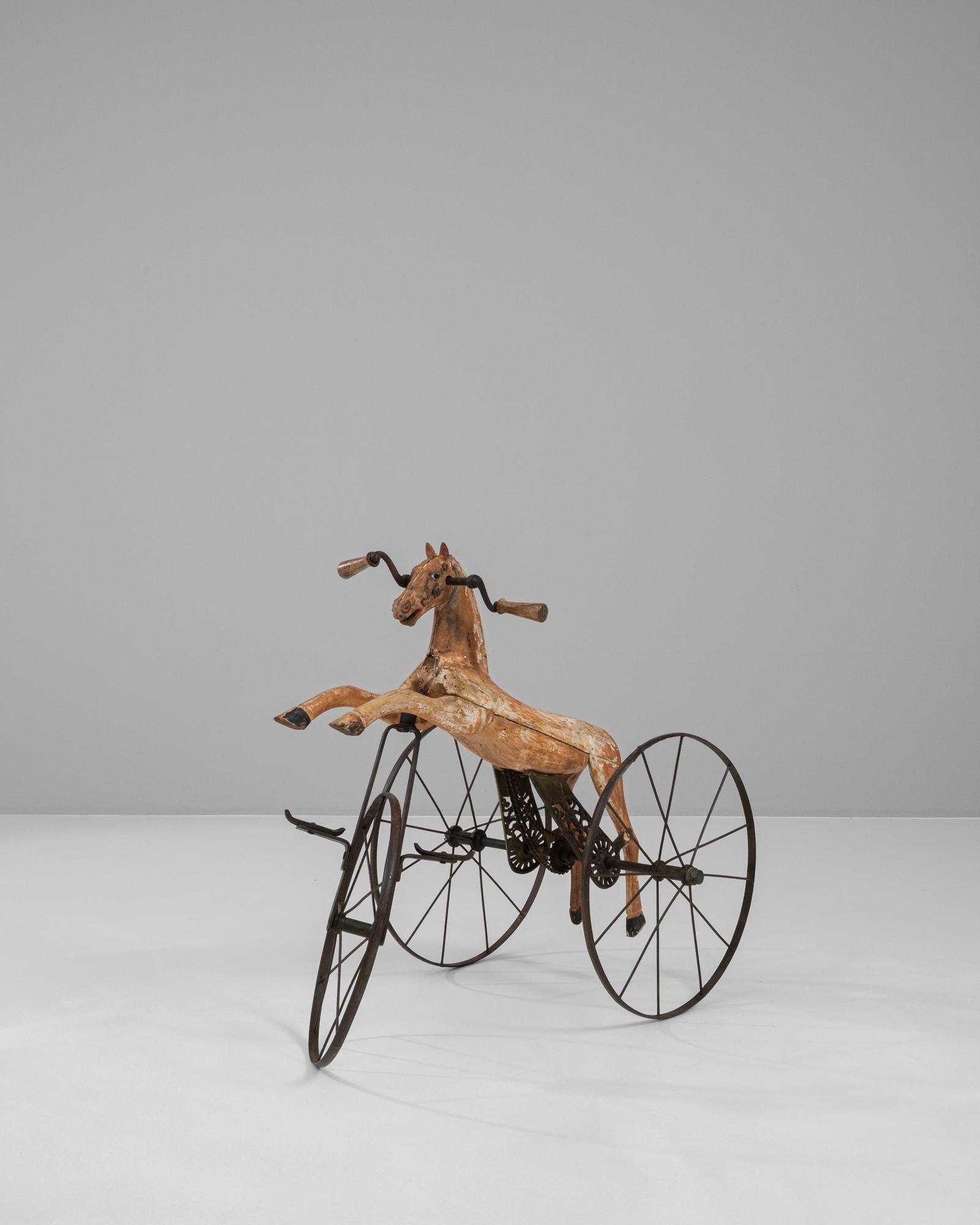 Step back in time with this exquisite 1900s French Wooden & Metal Horse Tricycle, a charming piece of history that is sure to captivate and enchant. Crafted during a bygone era of meticulous craftsmanship, this tricycle boasts a beautifully carved