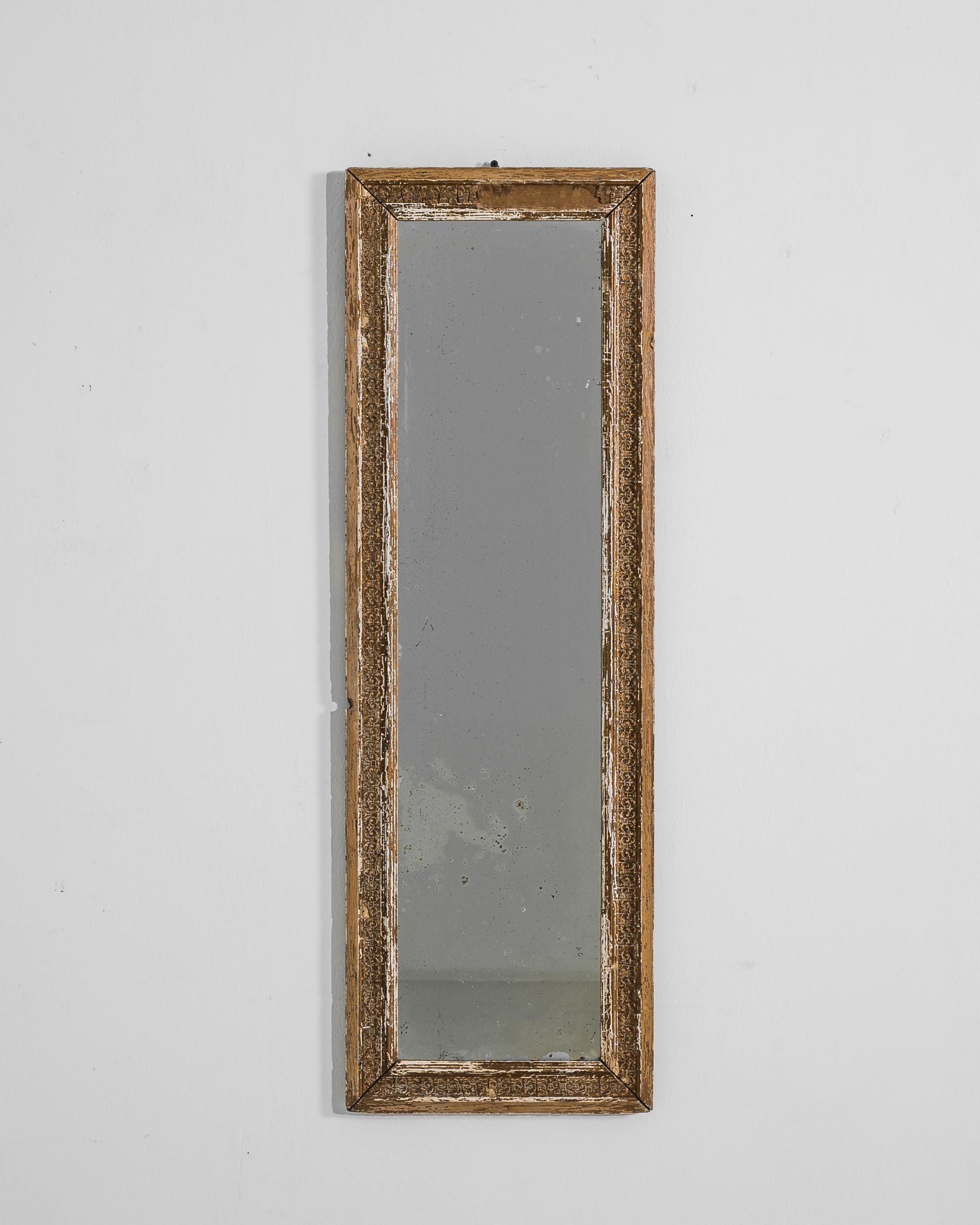 This 1900s French wooden mirror exudes an aura of vintage elegance with its distressed patina and ornate detailing. The weathered look of the frame, with its intricate carvings, tells a story of time passing—a decorative piece that not only reflects