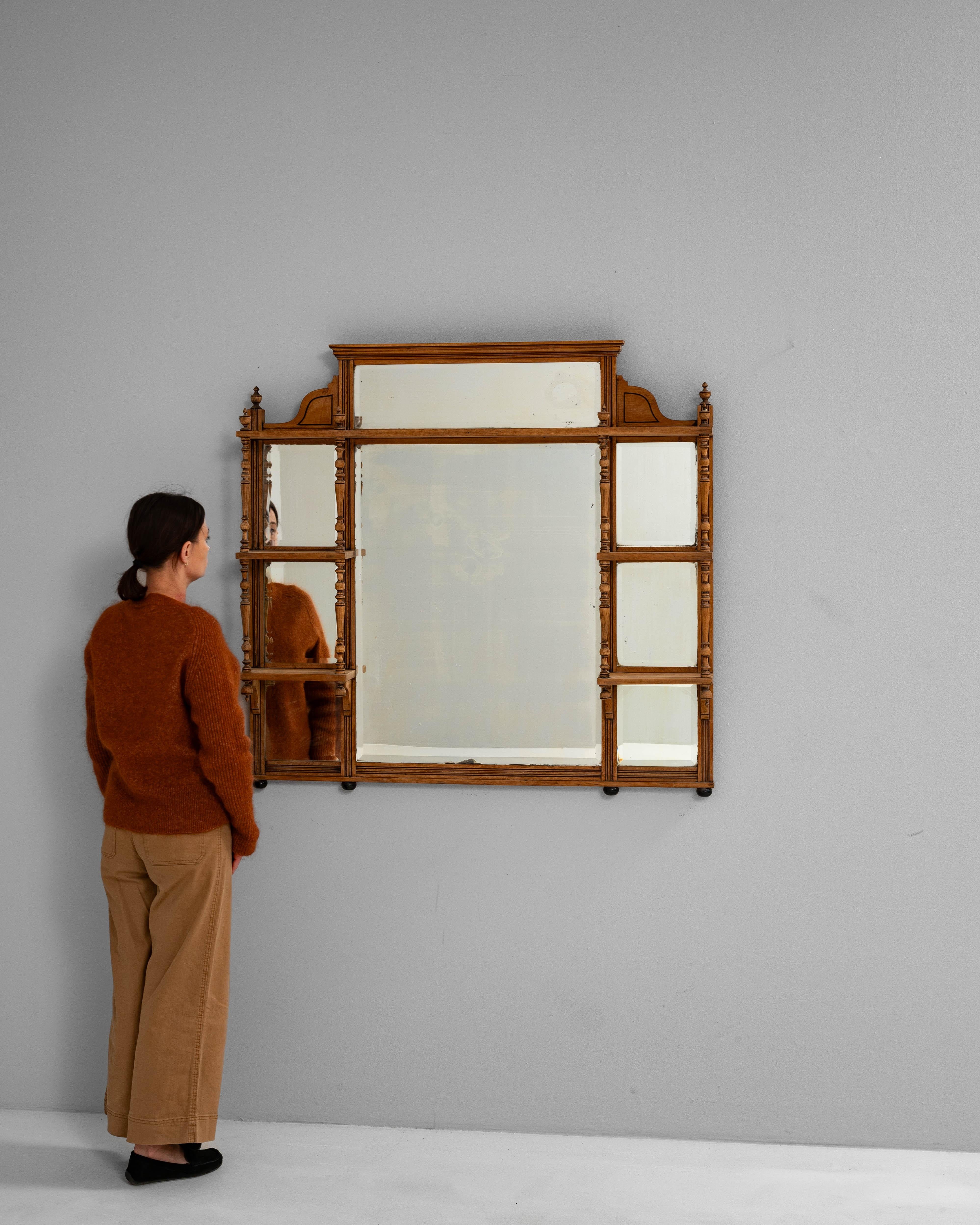 Ce miroir à trumeau français des années 1900 présente un cadre en bois chaleureux avec des étagères intégrées et des supports en fuseaux tournés, offrant à la fois un charme décoratif et un attrait fonctionnel. Le miroir est segmenté en plusieurs