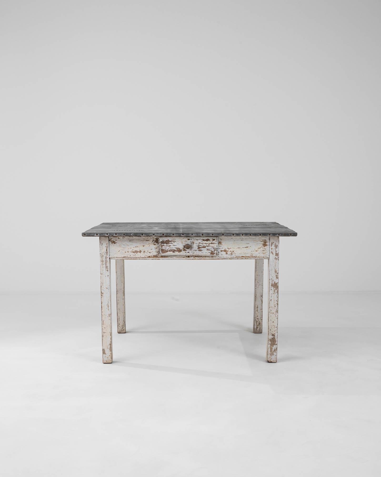 This early 1900s French wooden table with a zinc top exudes a sense of history and rustic charm. Its distressed white paintwork and weathered surfaces speak to its long-standing service and add a delightful shabby chic aesthetic to any space. The