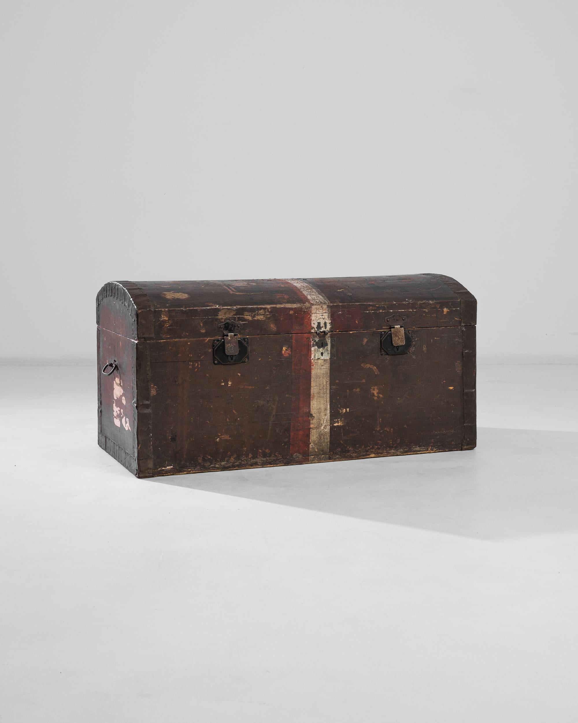 Dieser robuste, um 1900 in Frankreich aus Holz gefertigte Koffer verfügt über einen gewölbten Deckel, der die kantige Form des Koffers ausgleicht. Der weiß-rote Streifen, der in der Mitte der Kommode gemalt ist, spannt sie wie ein Band und bildet
