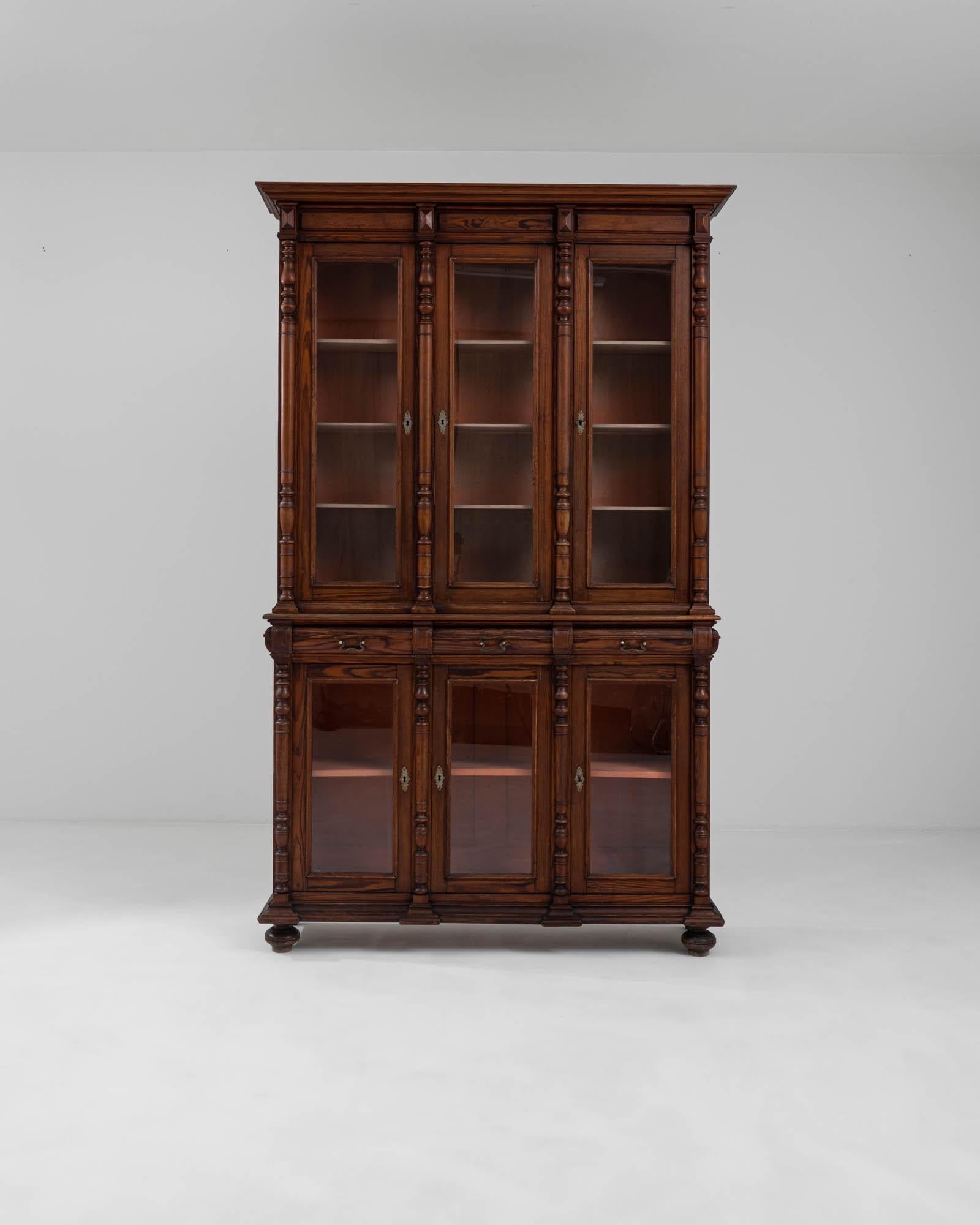 A wooden vitrine created in 1900s France. Towering above, this elegant find emits both an impressive display of elite craftsmanship and a warm and approachable familiarity. The semi-cylindrical columns that separate the shelves add a touch of artful