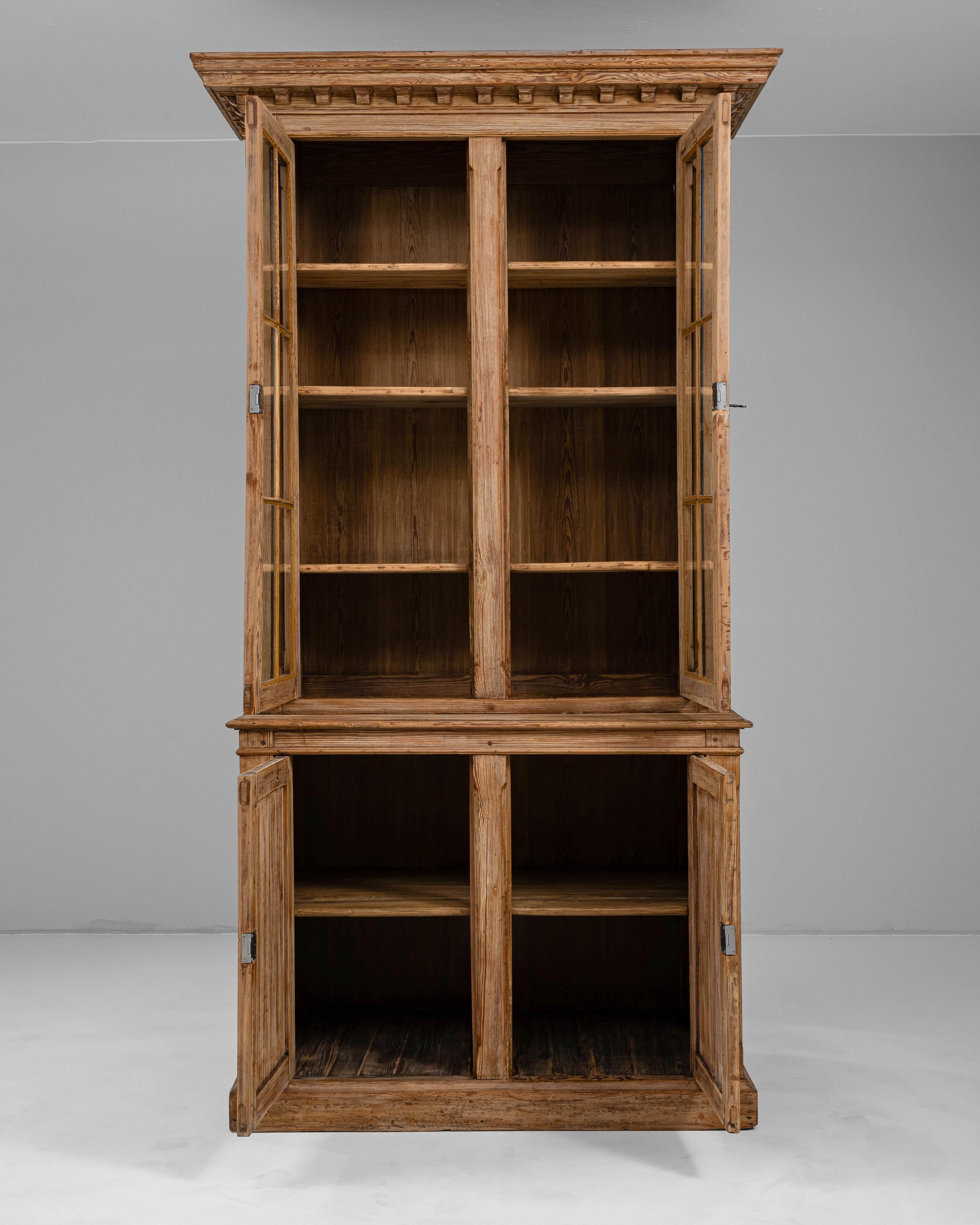 Questa vetrina francese in legno del 1900 offre un'eleganza senza tempo grazie alla sua silhouette maestosa e ai dettagli finemente lavorati. Realizzato in legno con una ricca venatura, il mobile in due parti presenta una sezione superiore con ante