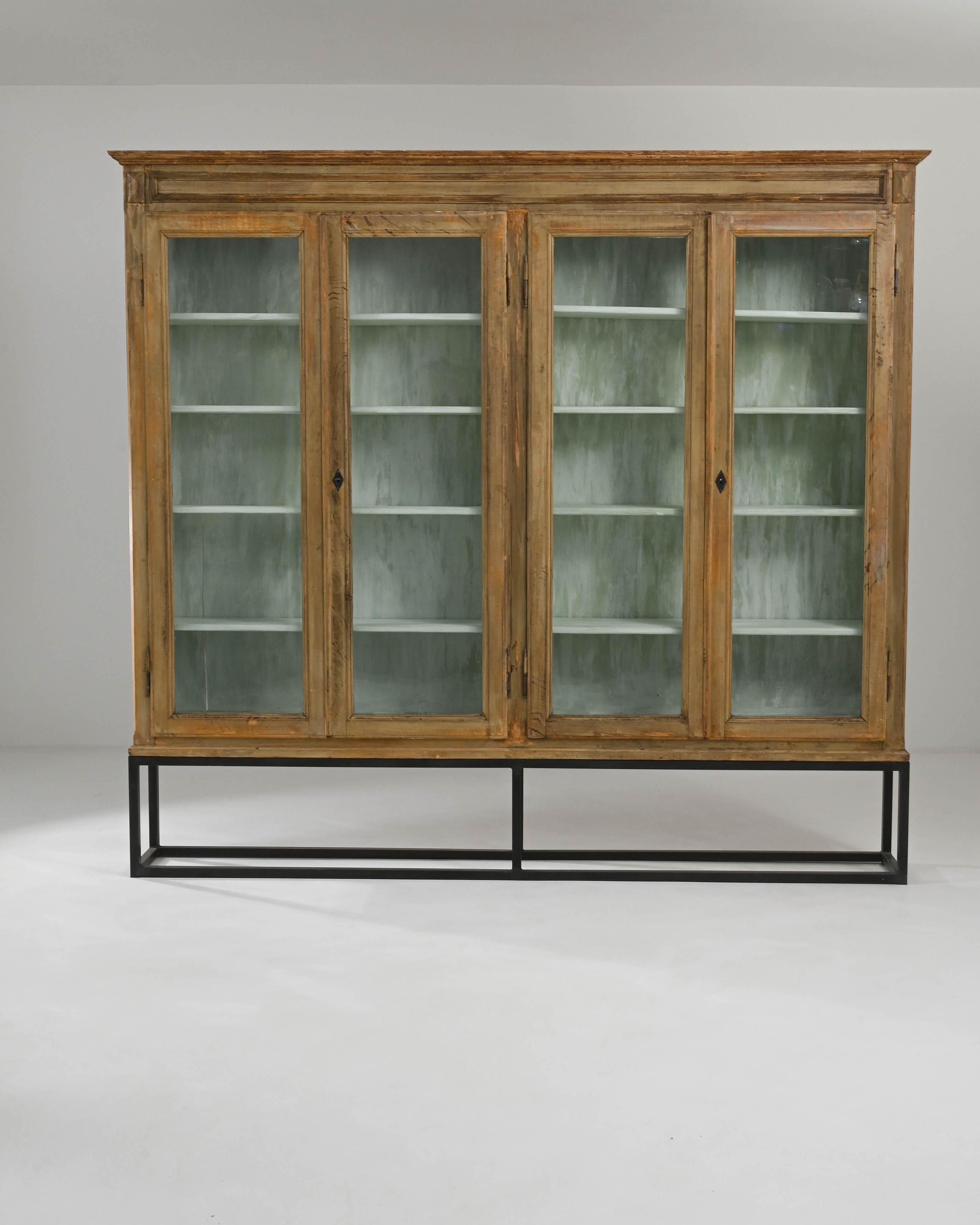 A wooden vitrine from France circa 1900 is mounted on a steel base. This imposing display case features two flanking pairs of glass paned doors which rise above the ground, stilted in the air by a geometric metal base. The cabinet's interior,