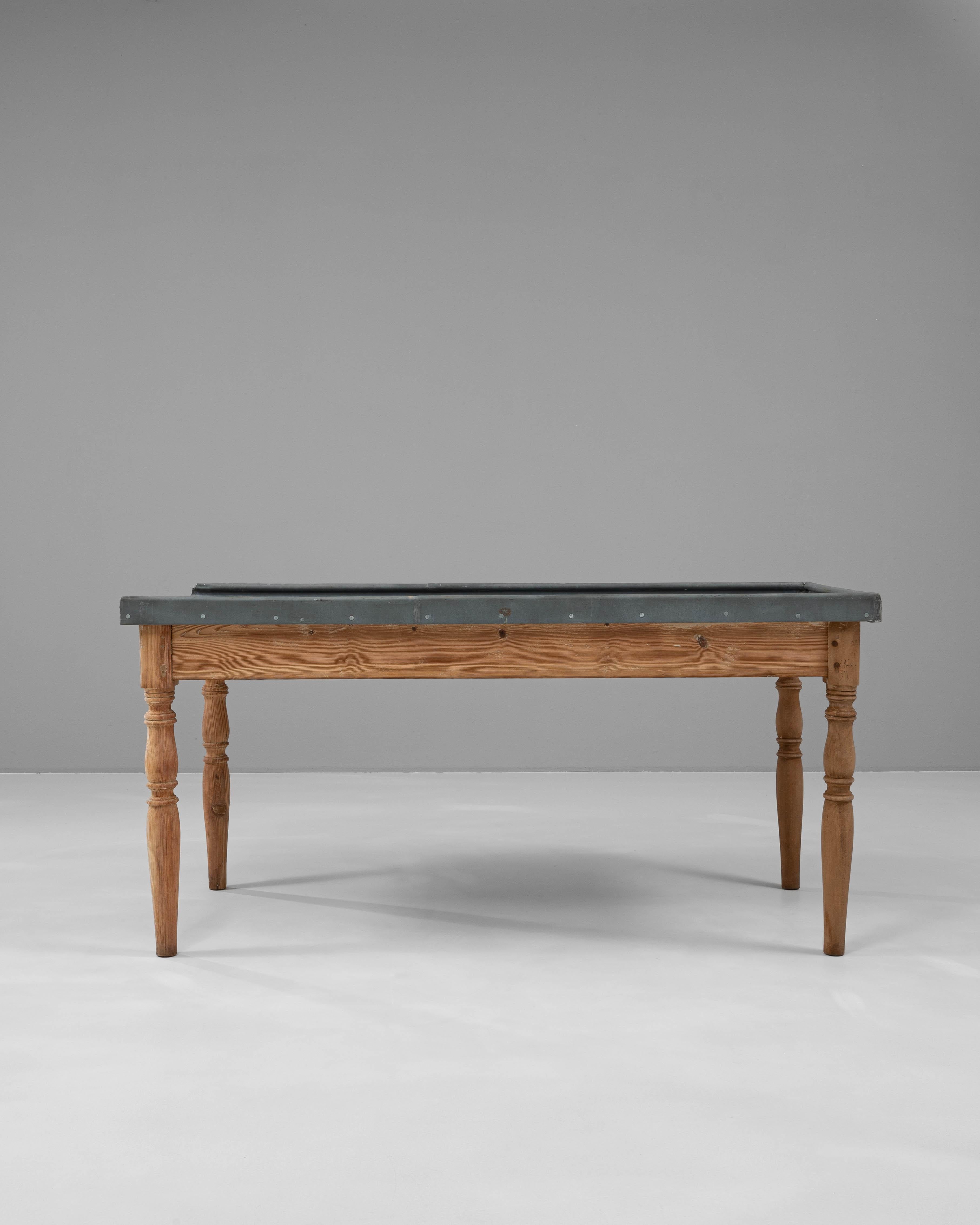 This early 20th-century French work table combines rustic craftsmanship with industrial functionality. The solid pine base features turned legs and a naturally aged patina that highlights the wood’s grain and warmth. Its zinc top, edged with