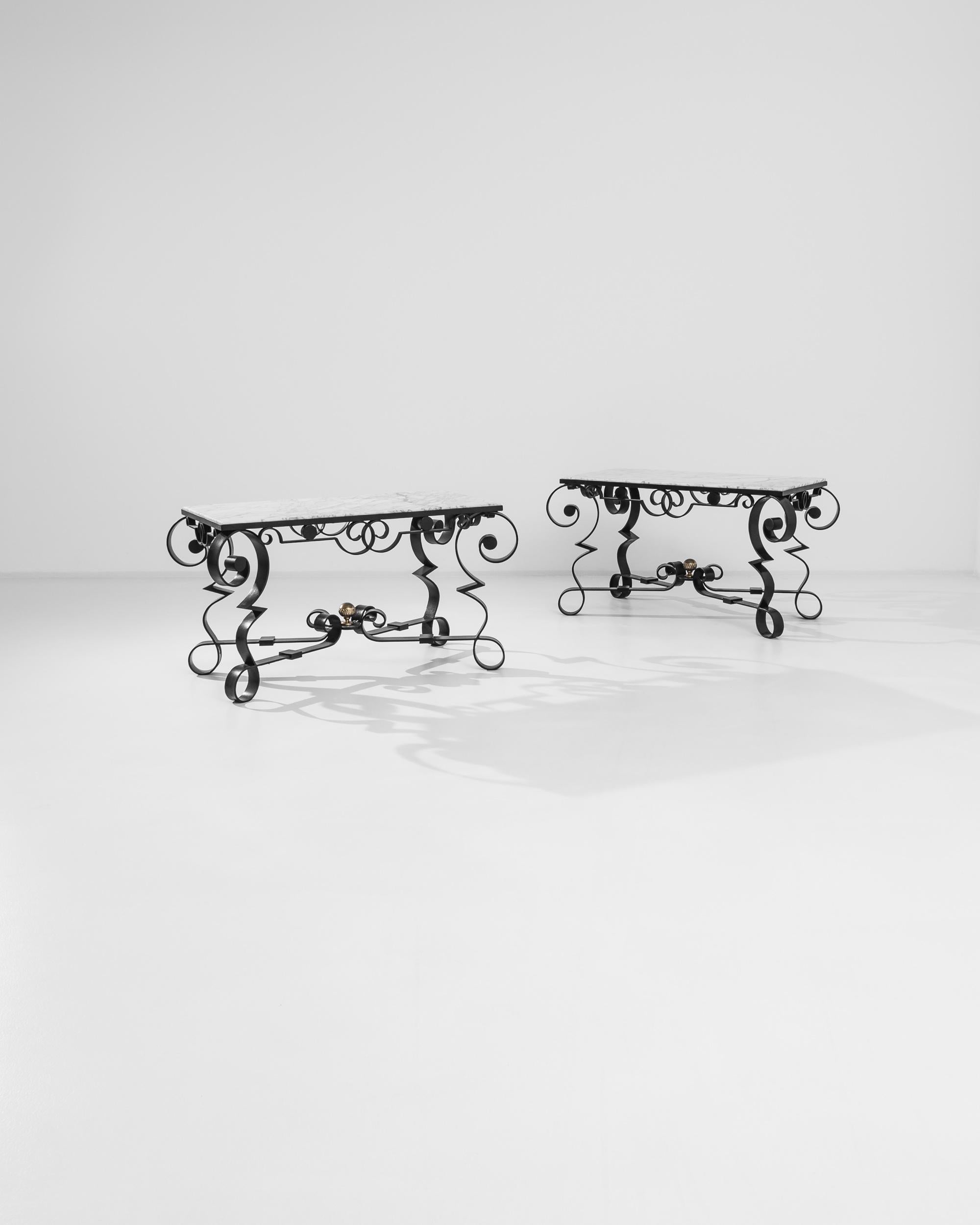 This pair of French tables was crafted, exquisitely, circa 1900. Their delicate gray marble tops rest over metal bases whose energetic swirls, twists and volutes create graceful silhouettes full of sensuous richness. An “X” shaped stretcher connects