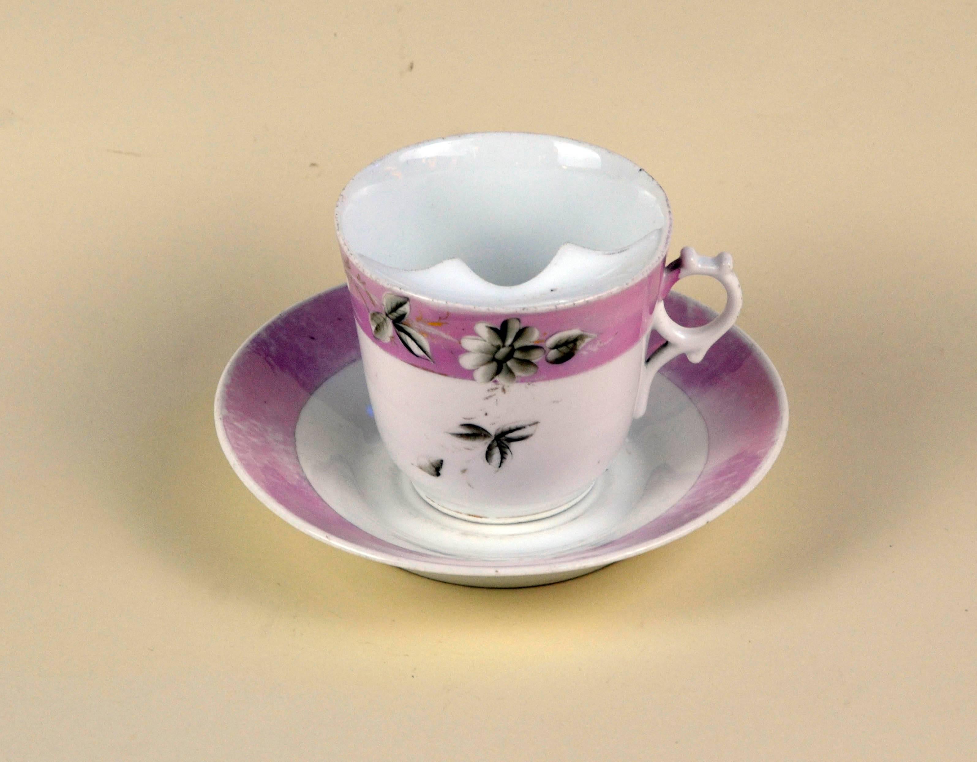 German white porcelain mustache cup finished with floral grey motive on an antique pink lustre band with matching saucer. 

Collector's note: 

The moustache cup (or mustache cup) is a drinking cup with a semicircular ledge inside. The ledge has