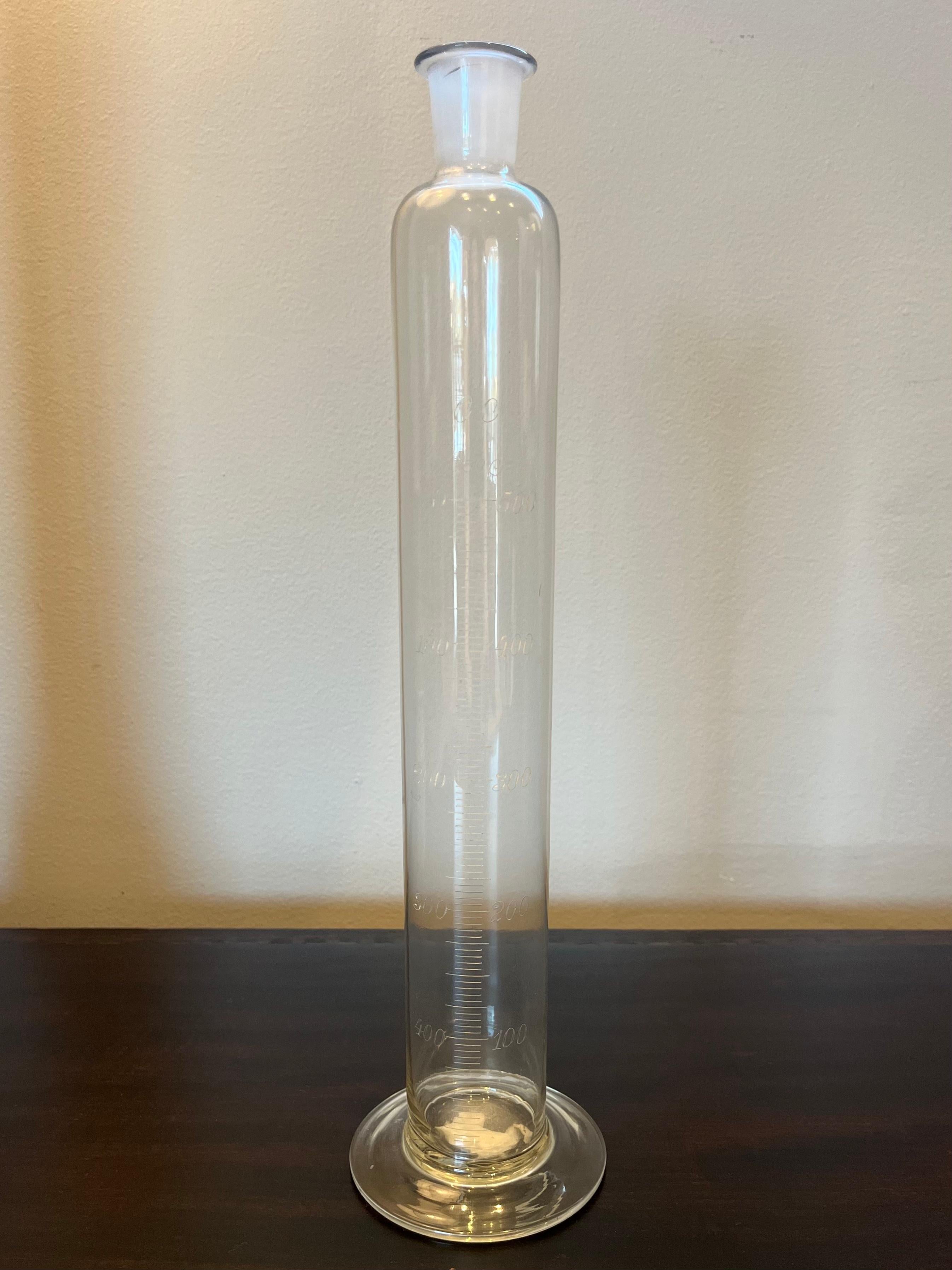 Glass chemist's beaker from 1900s France. The beaker has a cylindrical shape, small bottle neck and circular base with markings for various measurements. The engraved script is remarkably elegant and delicate. A wonderful example of an early