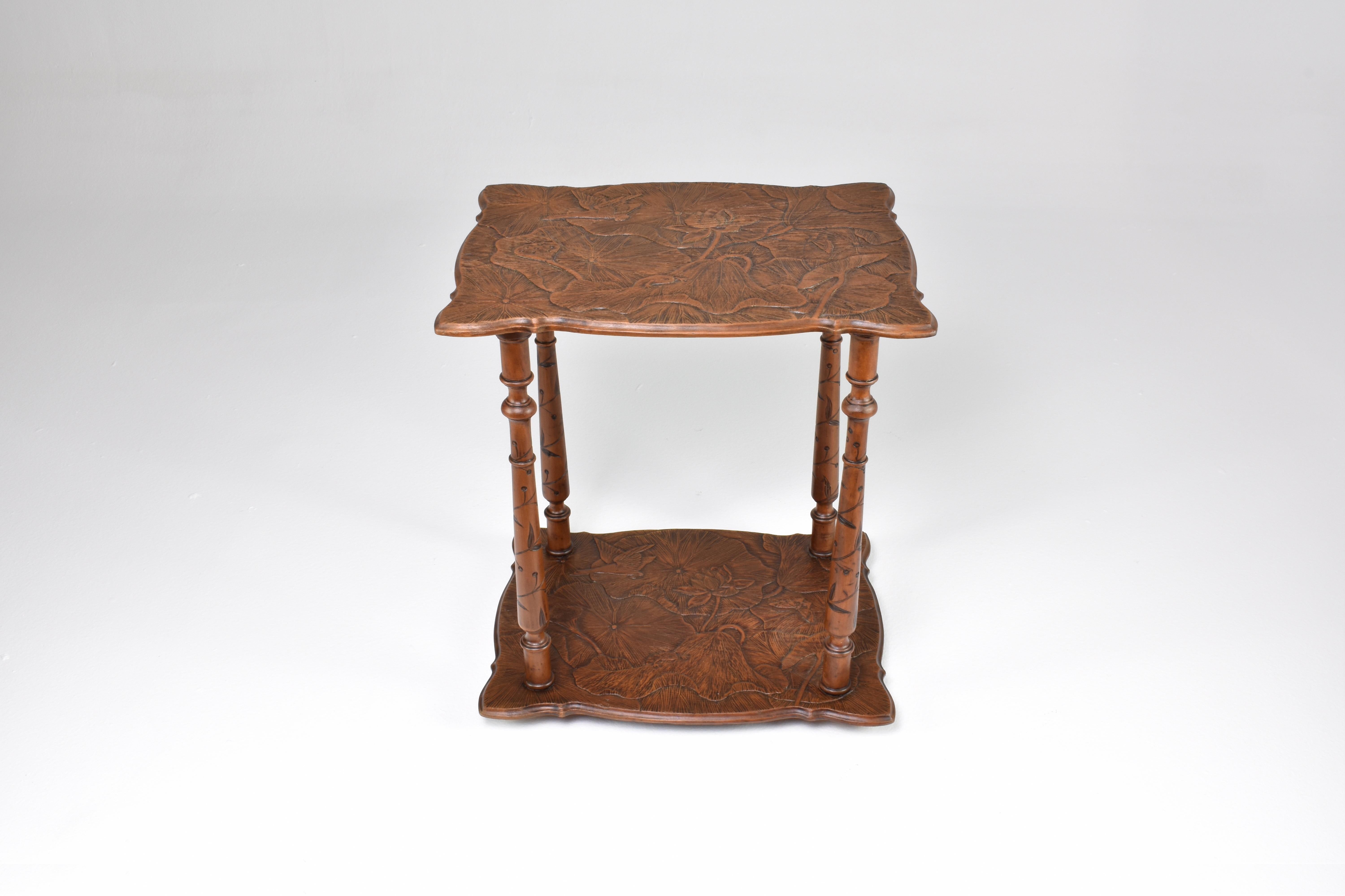 Experience the elegance of this tea table, reminiscent of the distinguished designs imported by the English firm, Liberty and Co., around 1900 from Art Nouveau Japan. Boasting intricately carved floral elements on both tabletops, the frame is