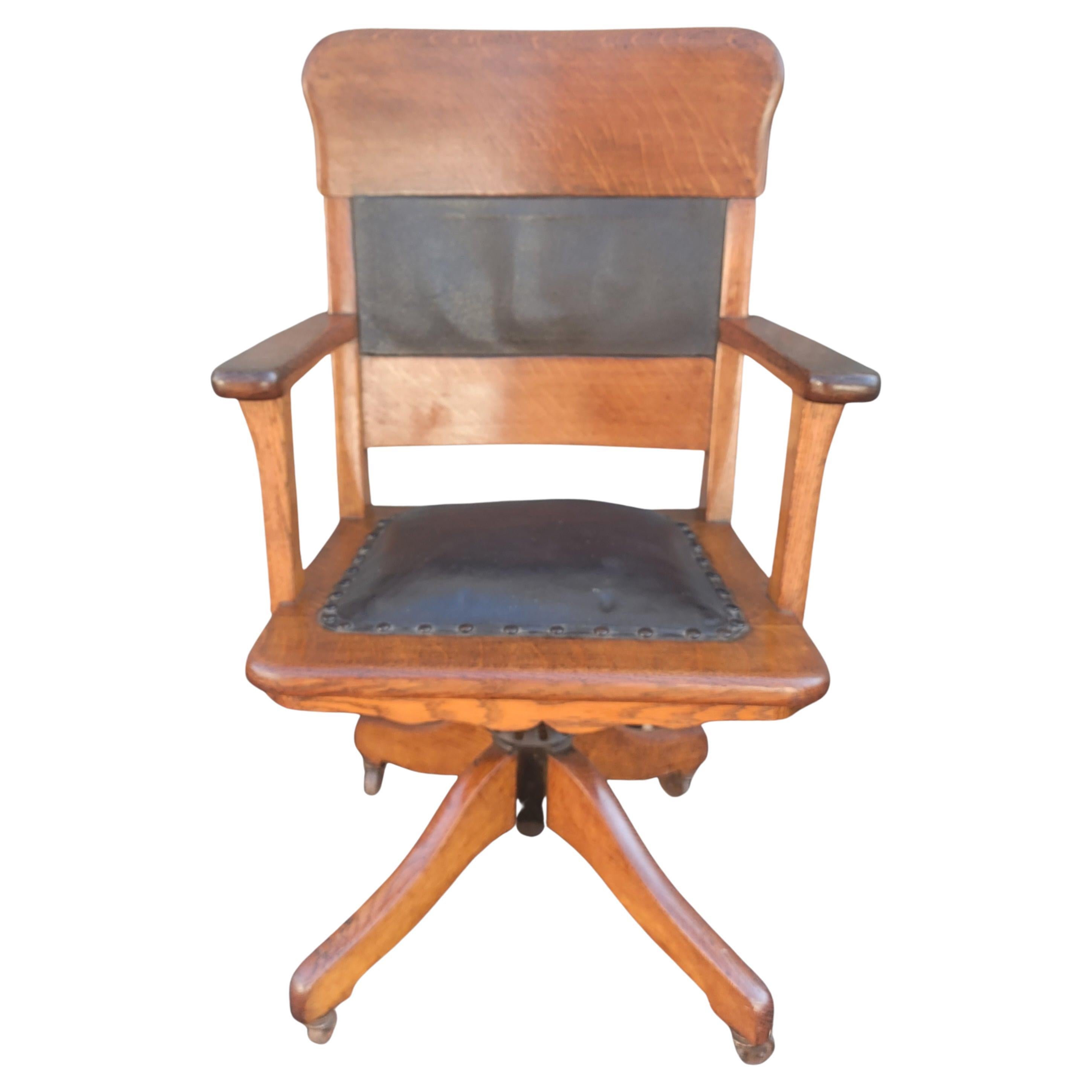 We are pleased to be offering this tiger sawn oak solid wood with leather seat and back lawyers/bankers swivel office chair that dates from the early 1900s in original condition. The chair is finished in a dark oak stain. It has shapely style arms,