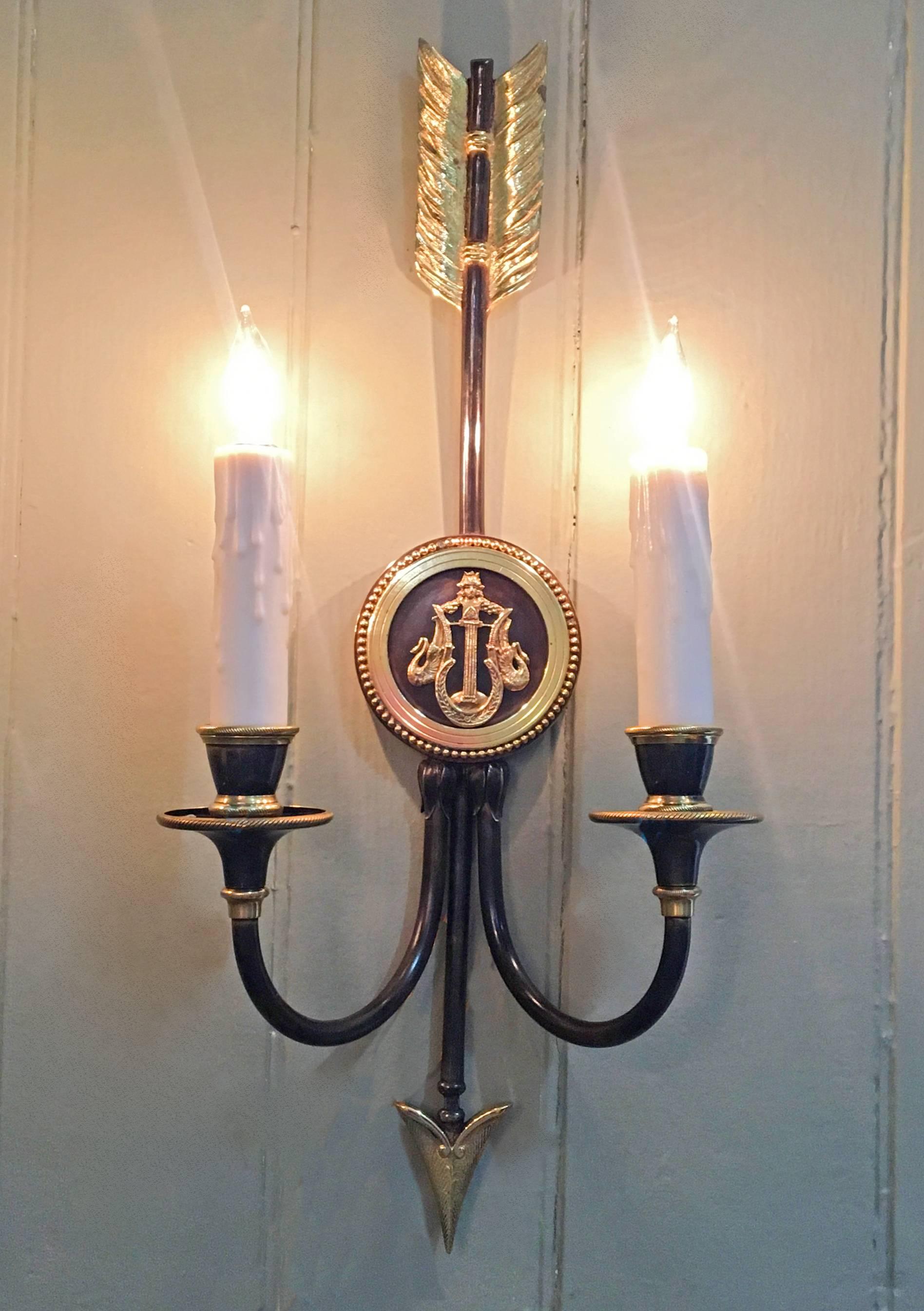 These 1900s regency arrow sconces are patinated and polished brass. The medallions on the sconces feature a lyre framed by swans with a grecian face. The sconces have been stamped in the brass the letters G.F.W.
    