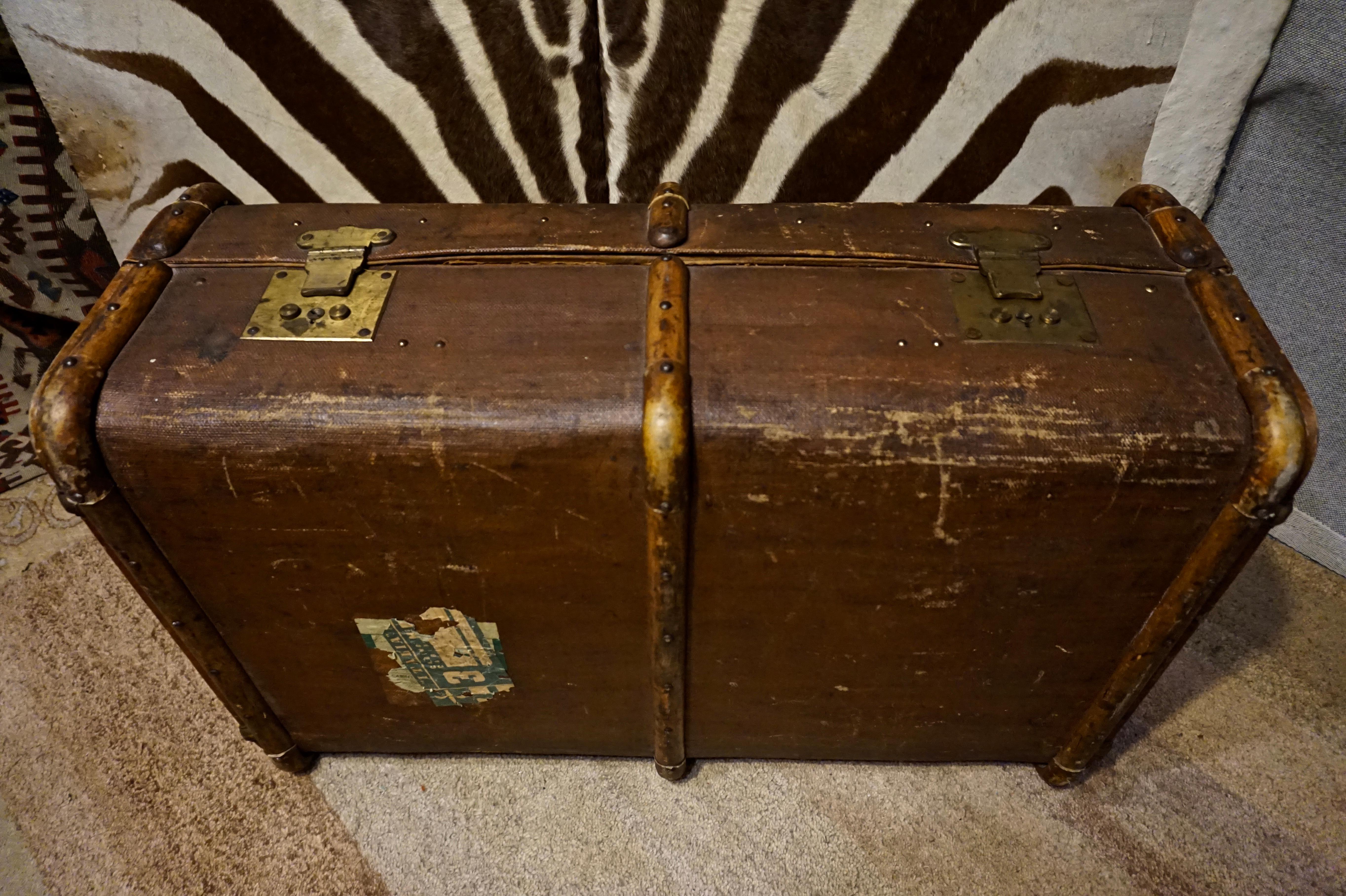 English steamer trunk which exudes old world charm and historic originality down to unrestored canvas, interior, travel stickers, leather work and wood trim, brass hardware and key. 