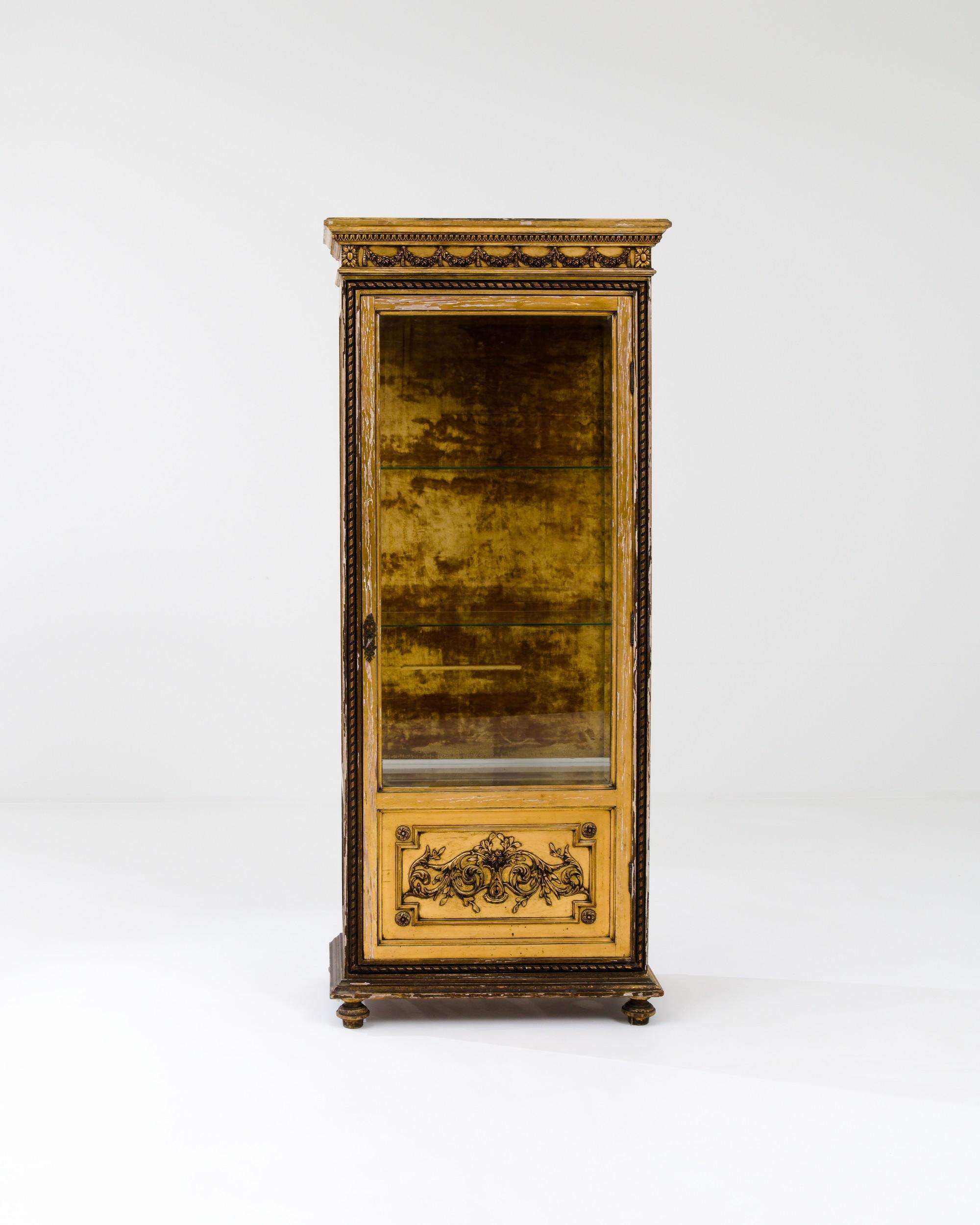 A wooden vitrine created in Spain circa 1900. Glowing with a historical luster, this tall and slender display cabinet dazzles with its time-earned details and painstakingly carved illustrations. Lavishly sculpted details punctuate the top, bottom,