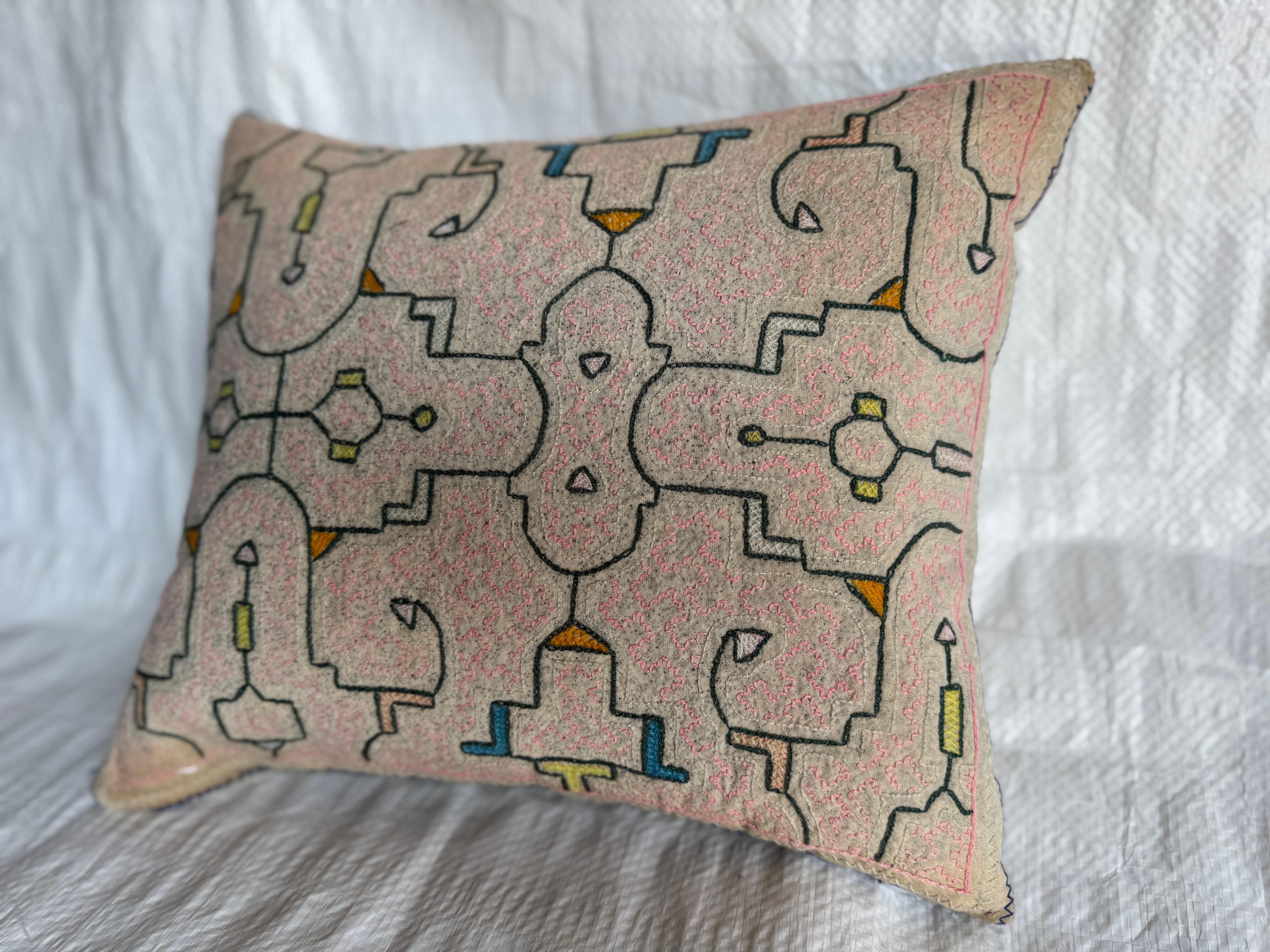 Questo cuscino antico è stato realizzato con un tessuto ricamato a mano risalente agli inizi del XX secolo. Il motivo presenta un disegno simmetrico e geometrico con influenze tribali, lavorato nei toni del rosa blush accentuati dal giallo e