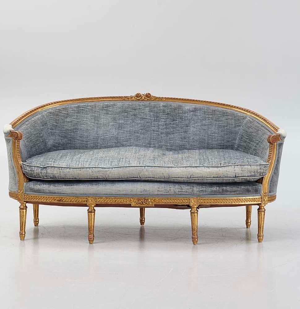 This wonderfully large and comfortable Swedish two seater gilt sofa dates from the 1900s period and is designed in the Gustavian style.
The sofa features classic scrolling decoration with carved flowers and leaves at the centre and has a slightly