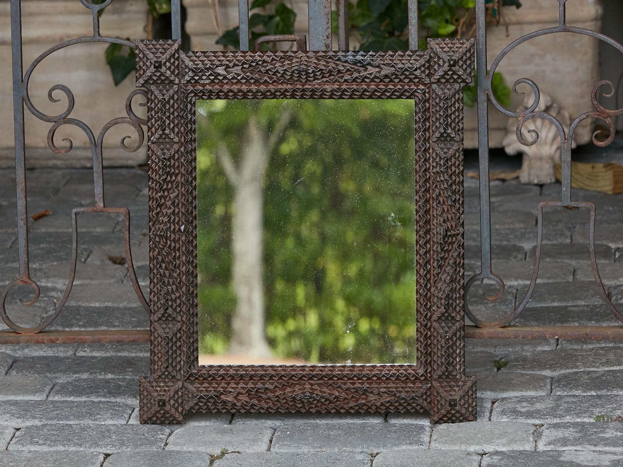 A French Tramp Art mirror from the Turn of the Century with protruding corners, raised geometric motifs and dark brown color. This exquisite French Tramp Art mirror, hailing from the Turn of the Century, showcases a striking blend of craftsmanship