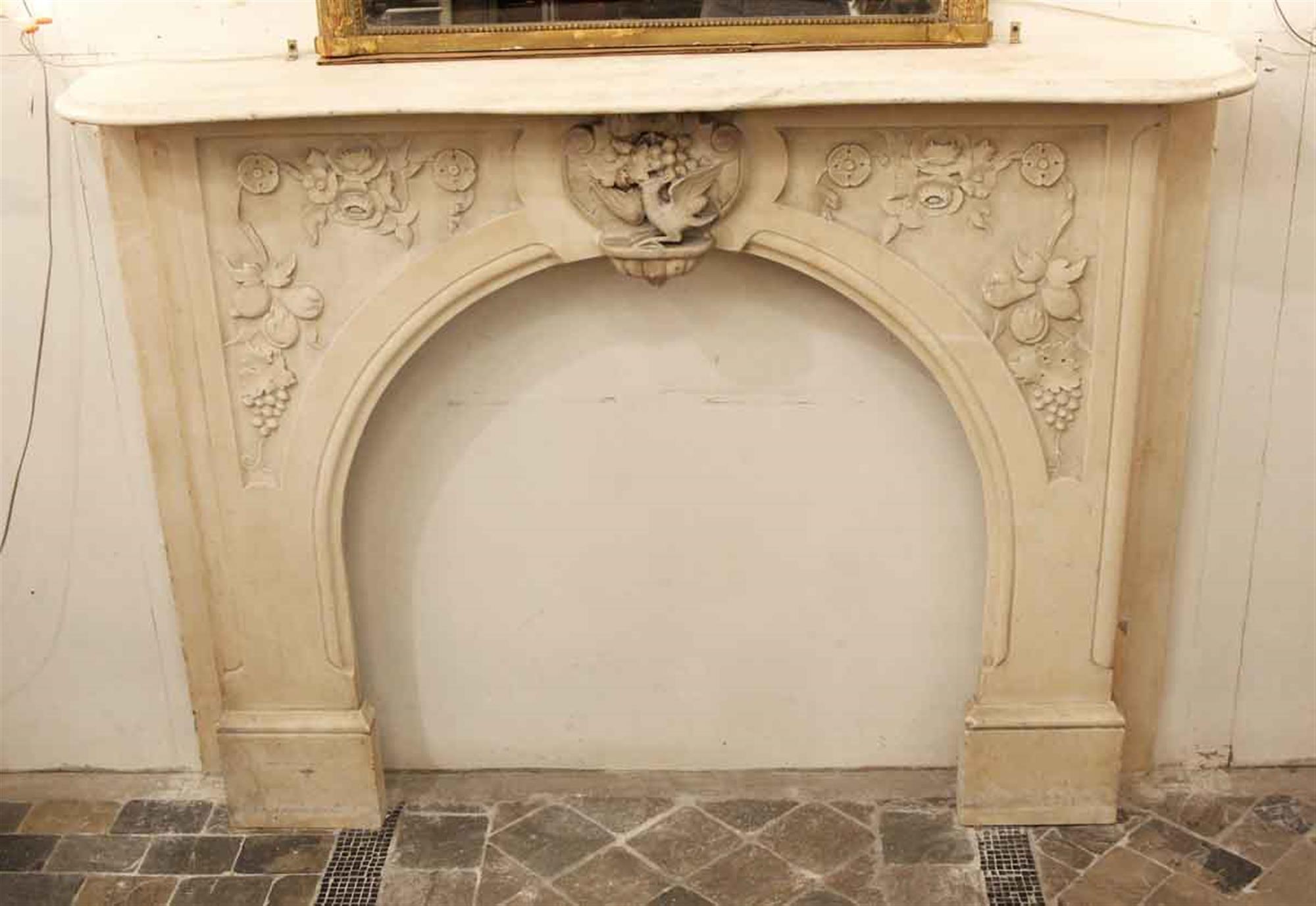 1900s tan Victorian hand carved marble mantel with grapevine, bird and floral details with an arched opening. This can be seen at our 333 West 52nd St location in the Theater District West of Manhattan.