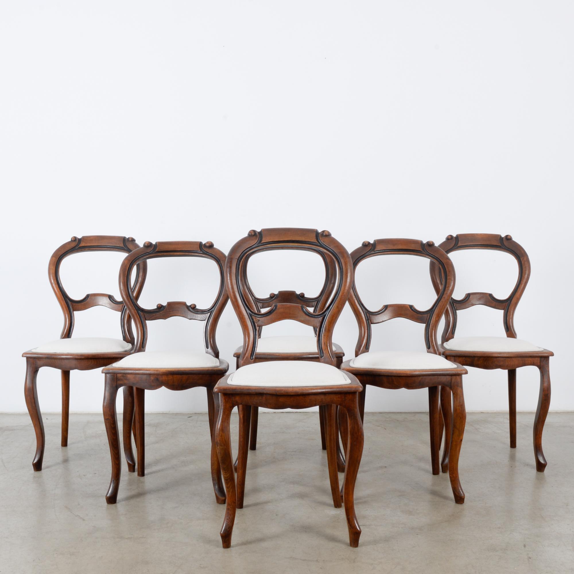 This set of six wooden dining chairs was made in France, circa 1900. The cabriole front legs echo the balloon back, which features a darkened, rounded ridge. The rear legs splay outward slightly. A re-upholstered cream seat on each chair sets off