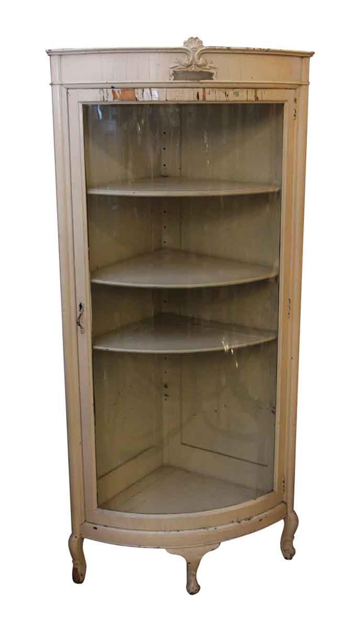 Painted white wooden cabinet with a glass front and three legs. The inside has three shelves. The top is stamped 