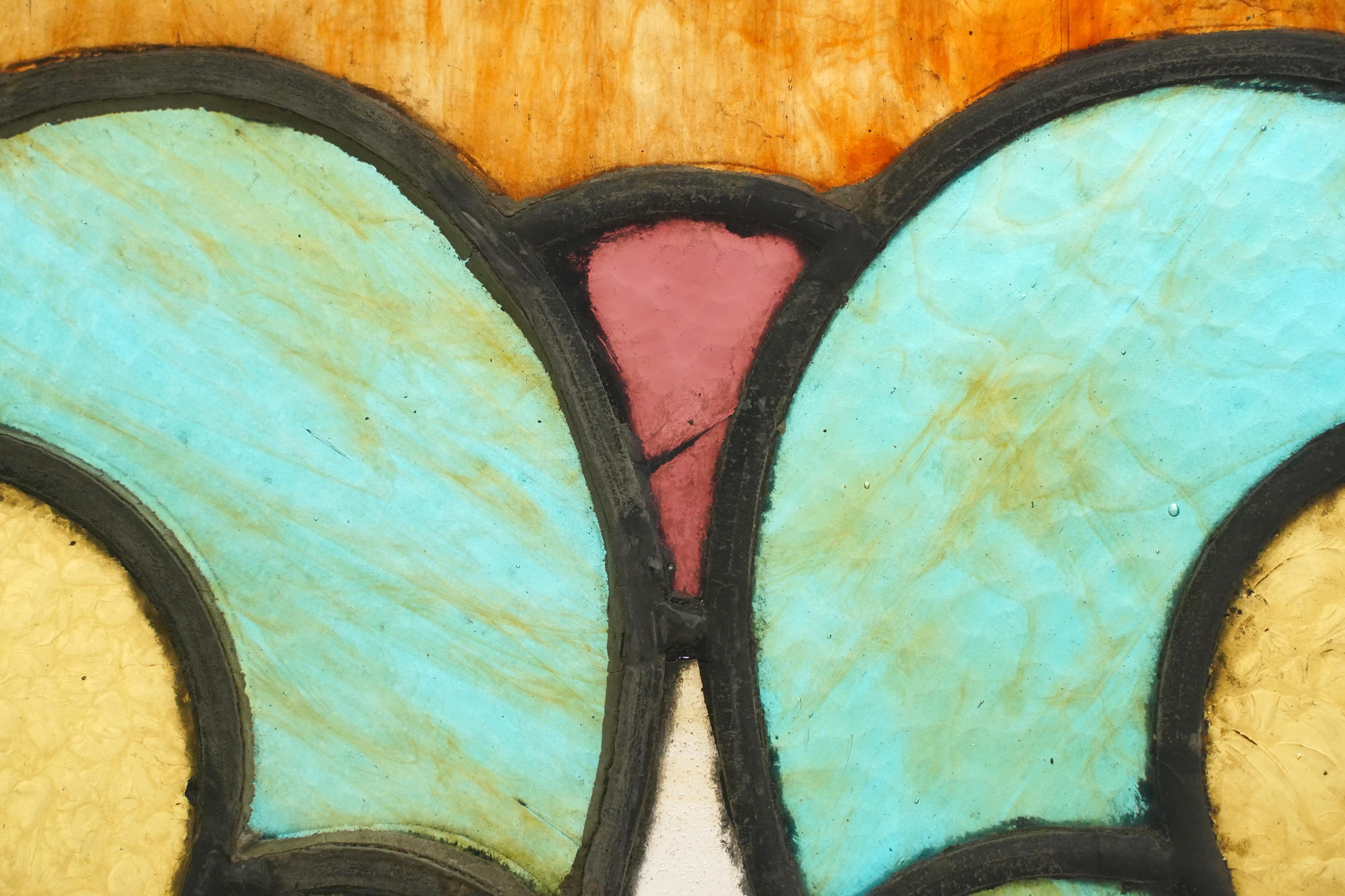 Antique rectangle church window with textured stained glass panels of yellow, amber, brown, and blue colors. The outside frame is painted a reddish-orange color, better known as terra cotta. The bottom window panel opens and has been protected with