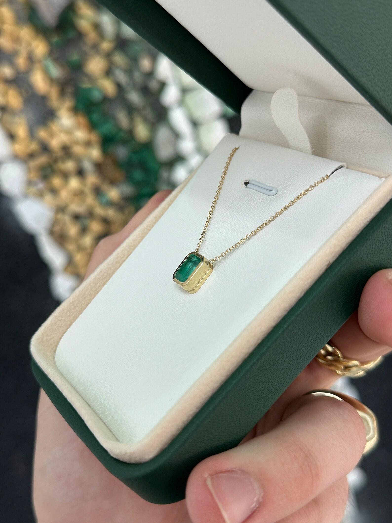 This stunning solitaire necklace features a vibrant medium green real emerald cut emerald, weighing just under two carats. The ethically sourced emerald is securely hand set in a sleek and modern bezel setting, which allows the beauty of the