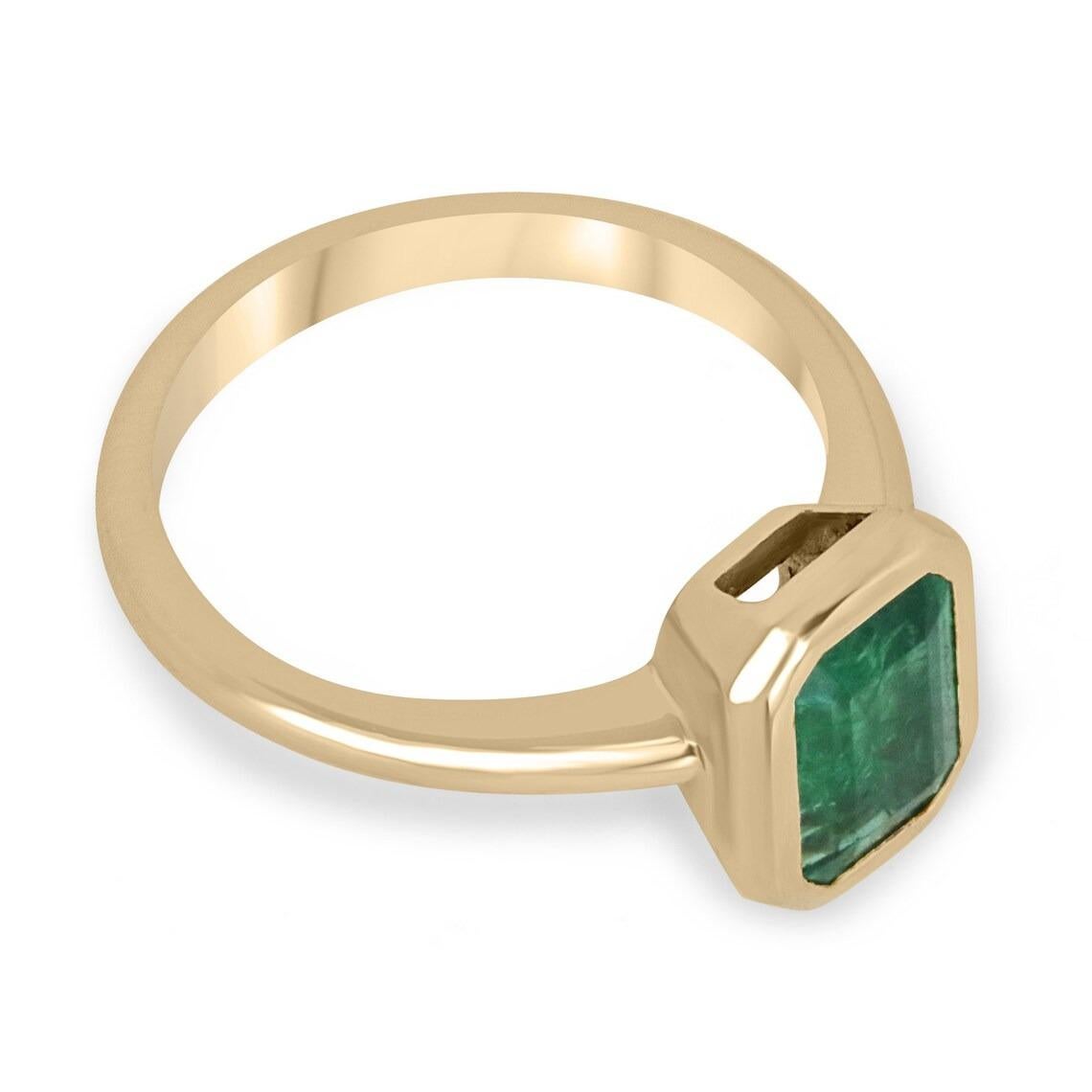 Displayed is a bespoke emerald solitaire emerald-cut engagement/right-hand ring in 14K yellow gold. This gorgeous solitaire ring carries an Emerald cut, emerald in a bezel setting. Fully faceted, this gemstone showcases excellent shine. The gem has