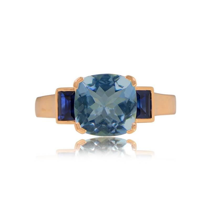 An elegant geometric ring crafted in 18k yellow gold showcases a prong-set, 1.90-carat cushion-cut blue topaz as its centerpiece. Adding sophistication, two natural baguette-cut sapphires are bezel-set on the shoulders.

Ring Size: 6.5 US,