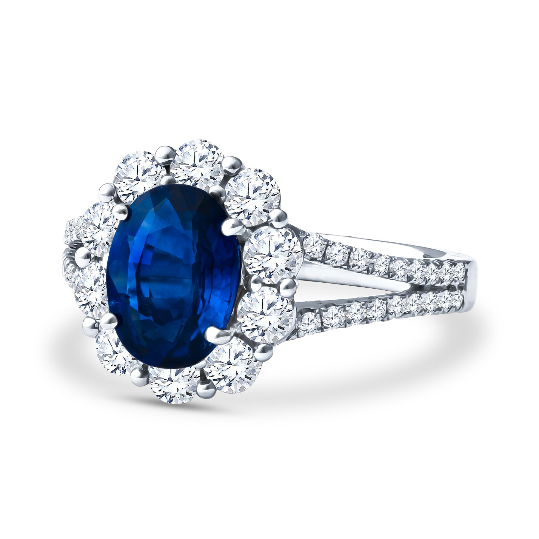 This stunning piece showcases a 1.90ct oval blue sapphire centerstone that is surrounded by 1.12ct total weight in round diamonds forming the halo and going down the split shank of the 18kt white gold ring. The ring is a beautiful floral shape,