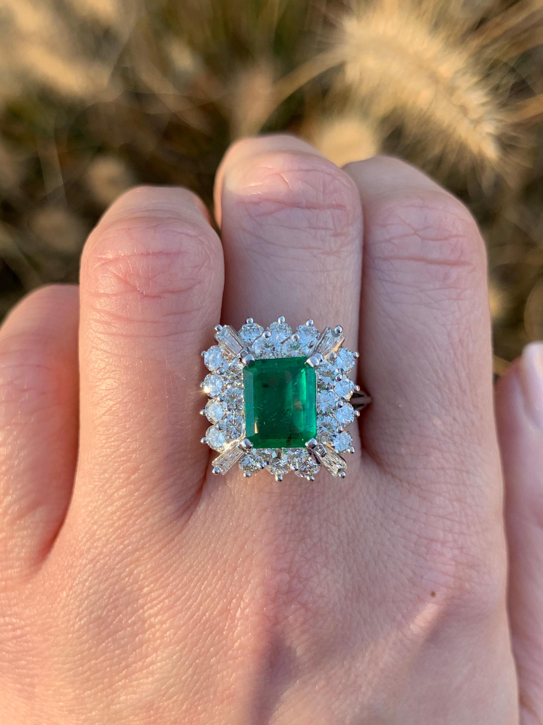 A gorgeous statement ring featuring a 1.90 carat emerald-cut emerald gemstone surrounded by two rows of high quality round brilliant diamonds, cornered with slender baguette diamonds. 24 Round brilliant diamonds have an approximate total weight of