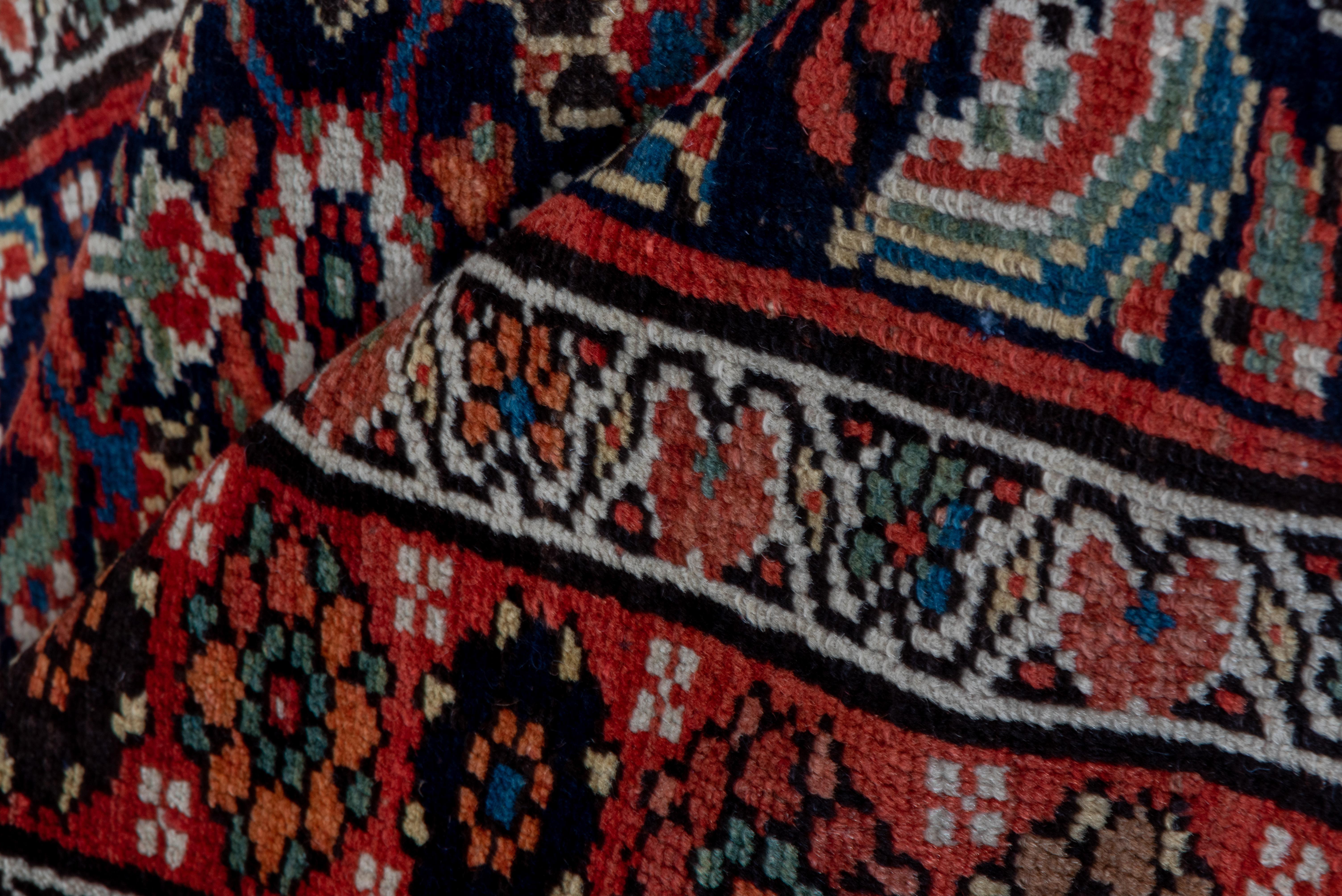This west Persian, cotton foundation kenare (runner) shows a dark blue field displaying a single column Herati design with salient ecru rosettes. Red, rust, light blue and teal accents. Red main border with vary coloured rosettes and attendant off