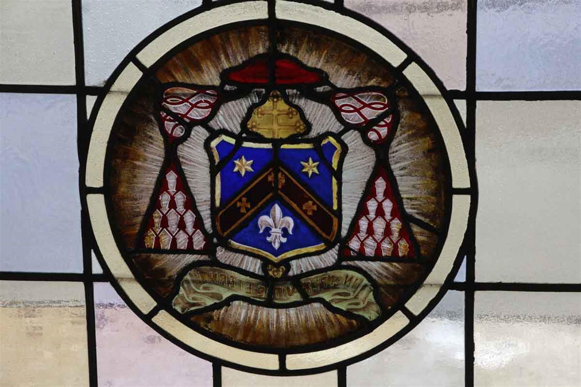 1910 Arts & Crafts wood framed stained glass window with a center shield, fleur de lis and star motif. The glass colors consist of soft hues of blue, green, pink and amber. Some stress cracks. This can be seen at our 400 Gilligan St location in