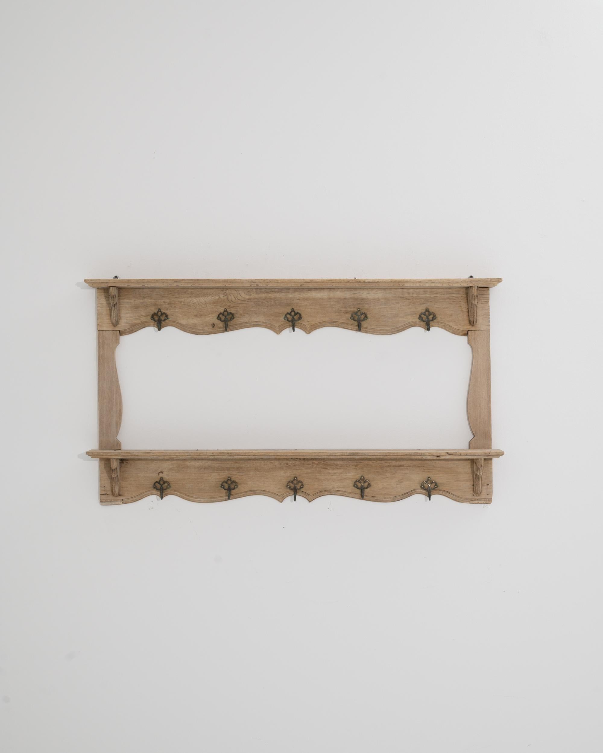A wooden wall rack, circa Belgium 1910. Lined with ten hooks, five on top for hats and scarves, and five below for jackets and coats, this charmingly rustic wall rack offers ample storage functionality. Gently carved scroll patterning and detailed