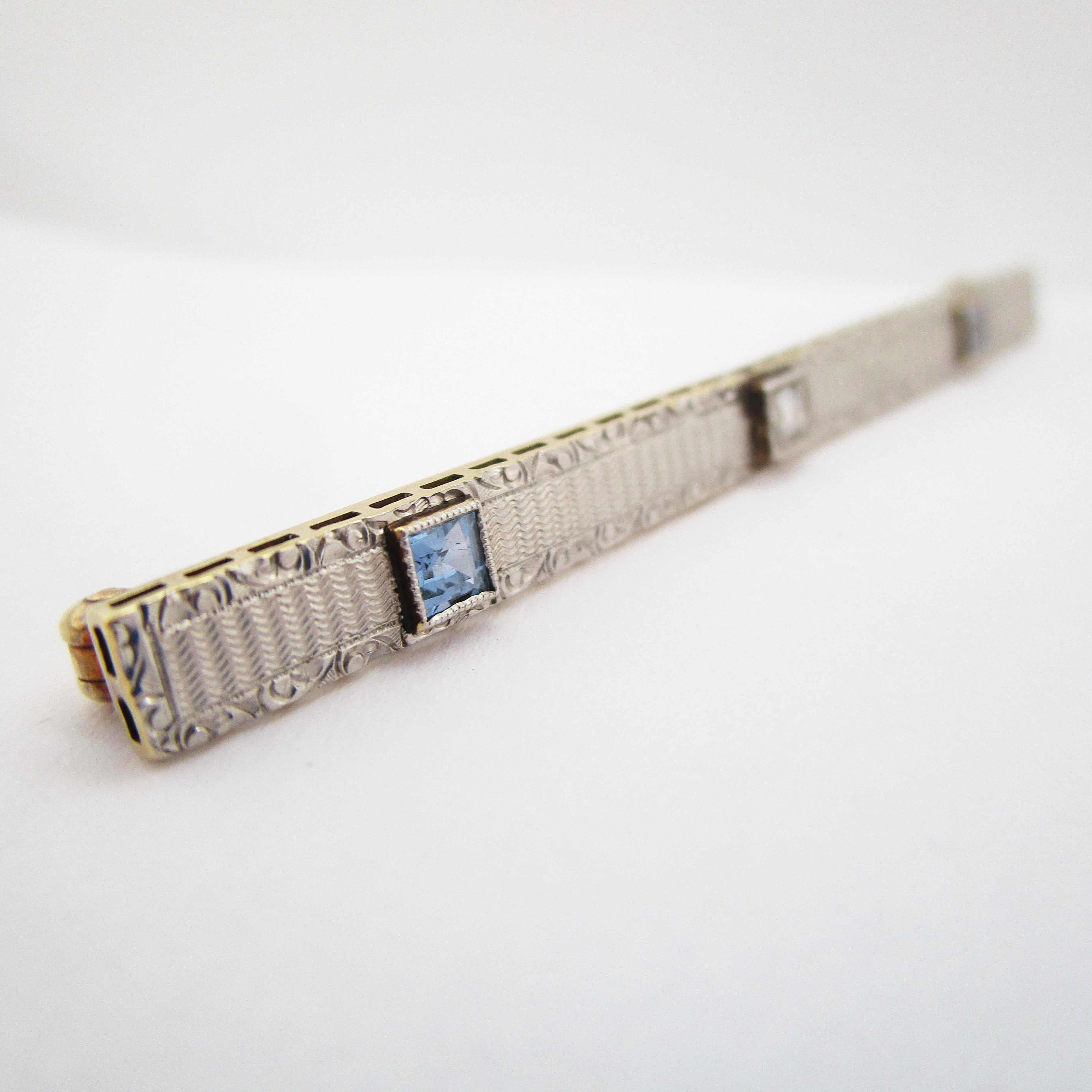 This stunning Edwardian bar pin features a brilliant combination of platinum over gold set with a bright white diamond and two gorgeous natural blue sapphires! The edges of the pin are hand engraved with a lovely scroll-like pattern that creates a